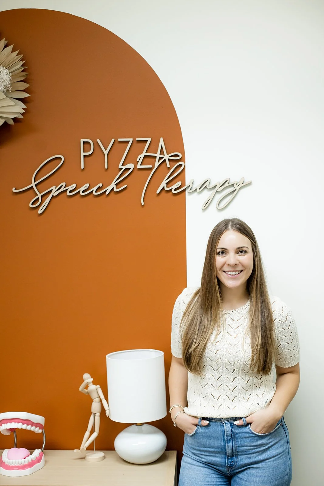 Gabby Pyzza, speech-language pathologist and author of the Pragmatic Language Handbook, standing beside the Pyzza Speech Therapy office sign