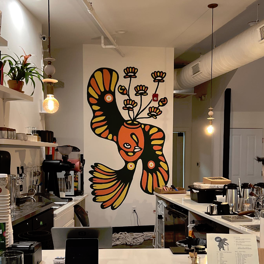 Colorful mural of a bird with flowers coming out of its head on a white wall in a cafe or restaurant.