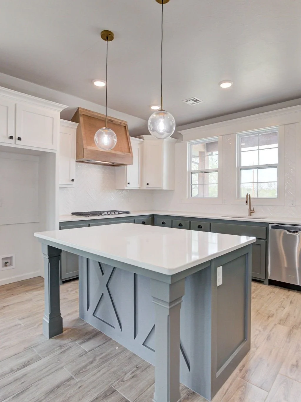 Modern kitchen with white upper cabinets, gray lower cabinets, a white countertop island, pendant lights, and a window above the sink.