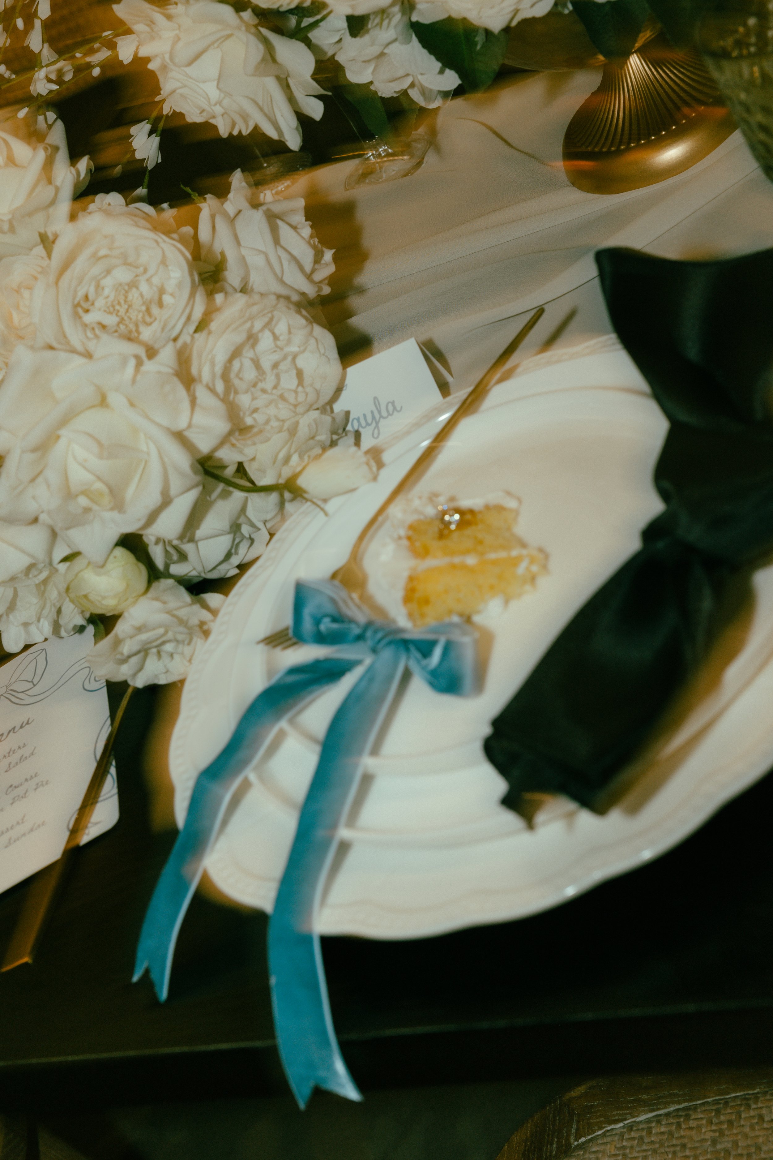 Elegant place setting with white flowers, a dessert plate, a fork, a name card, and a blue ribbon on a table.