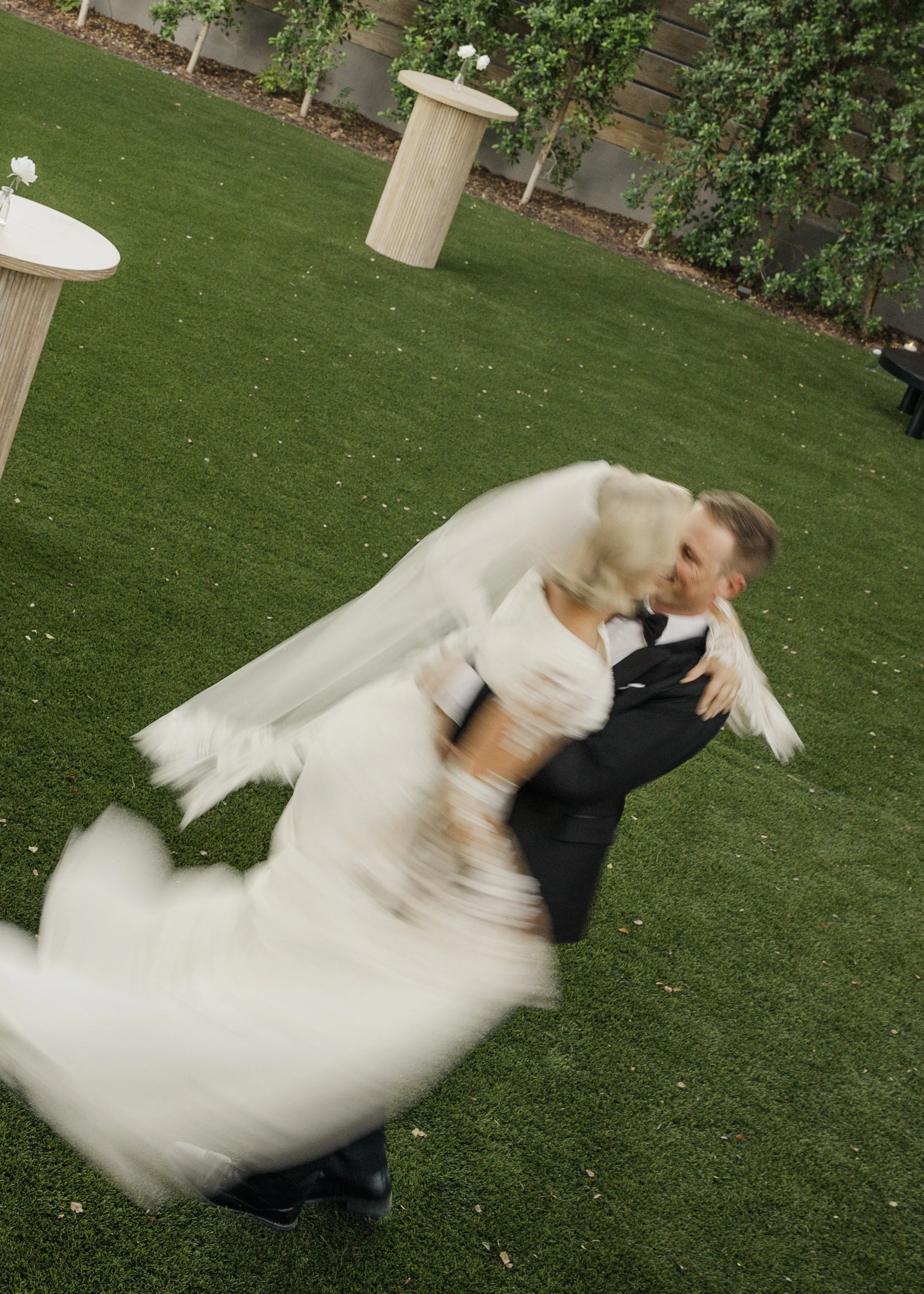 Bride and groom spinning on grass lawn, wedding attire, blurred motion.