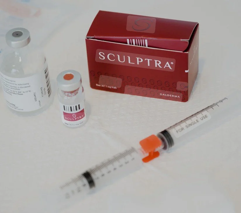 A red box labeled Sculptra with two small vials and a syringe on a white surface.