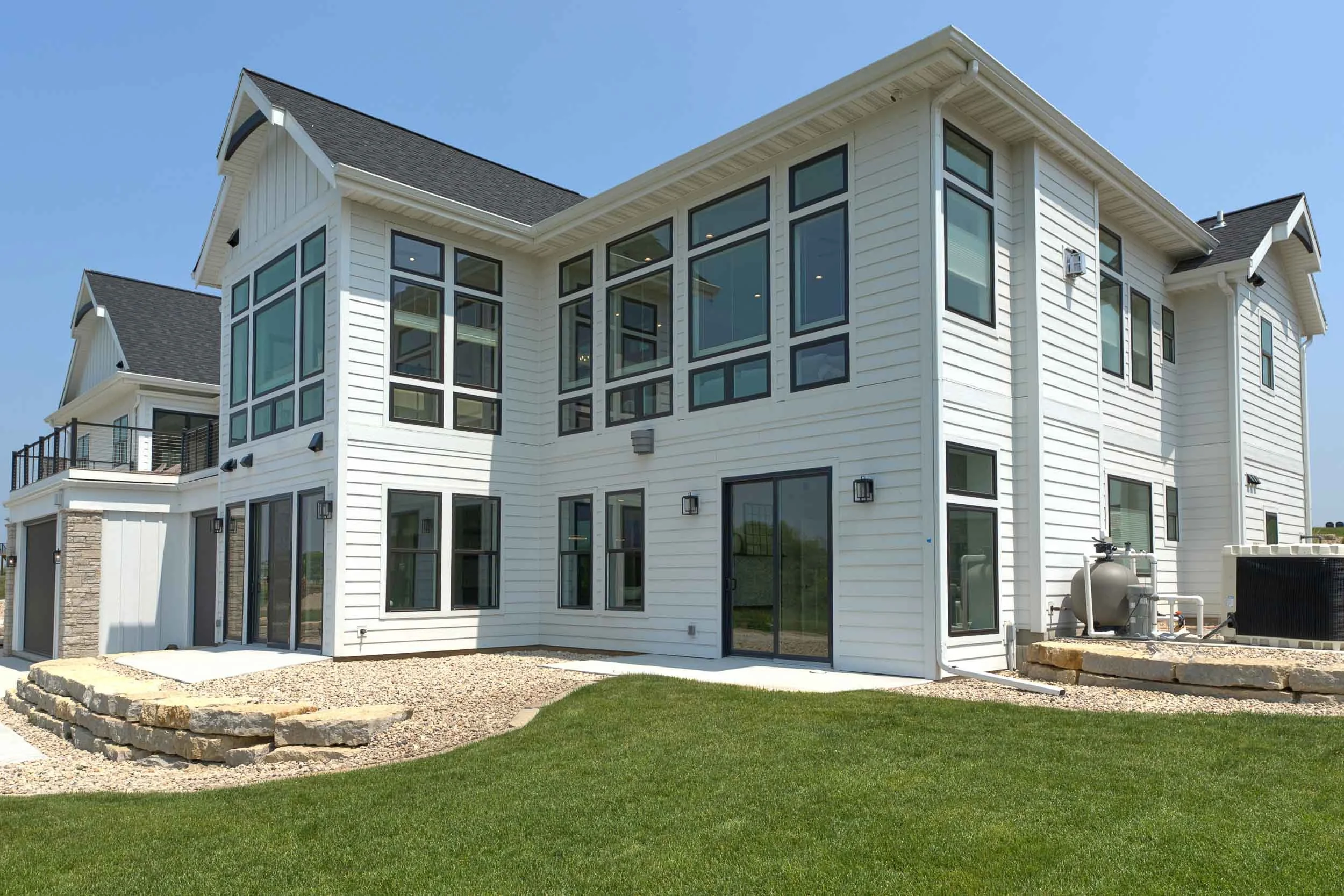 Modern white multi-story house with large windows, a backyard with a stone patio, green lawn, and a clear blue sky. Hardie board siding in Calgary