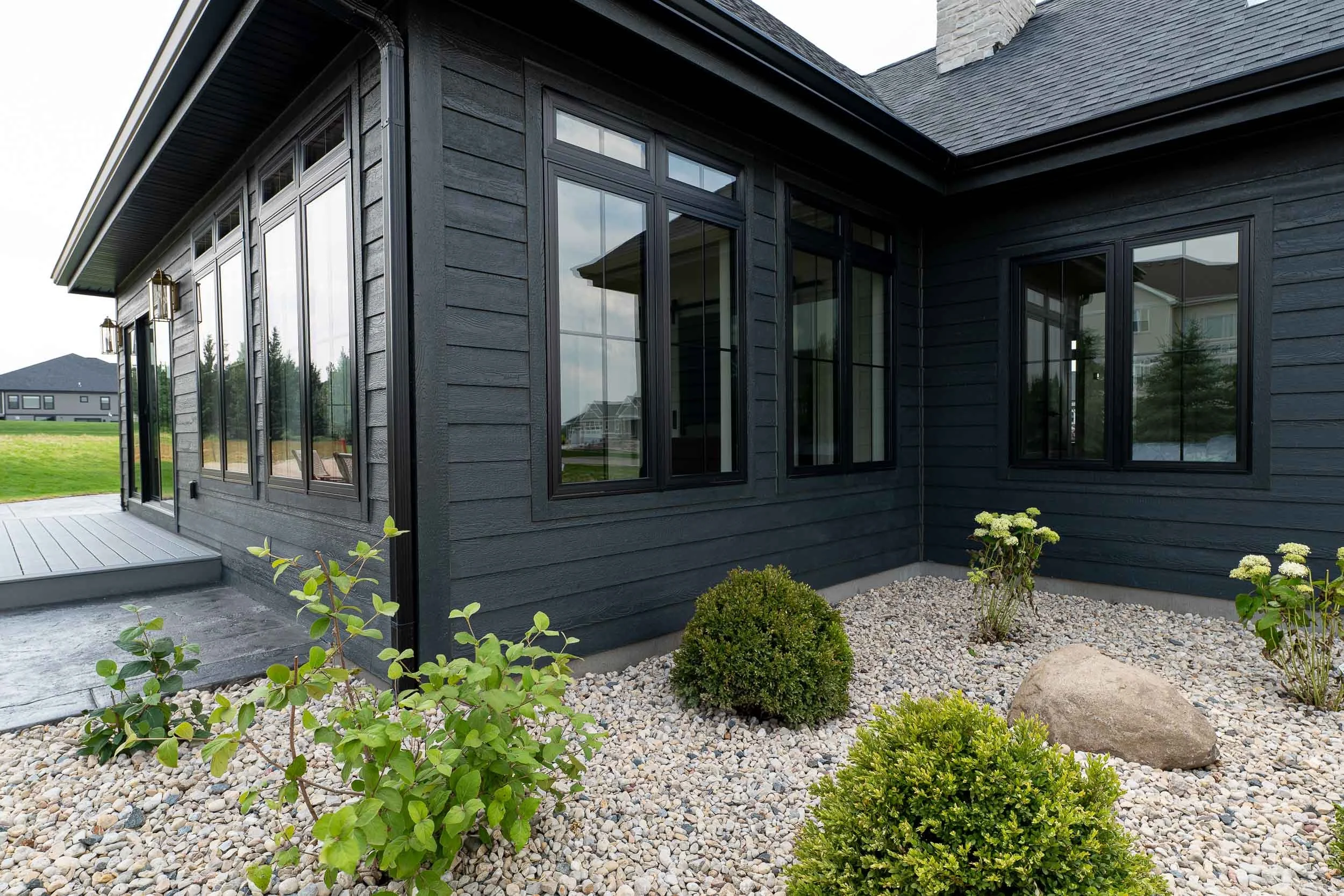 Exterior of a black house with large windows, gray gravel landscaping, and small green bushes. Siding installation in Calgary.