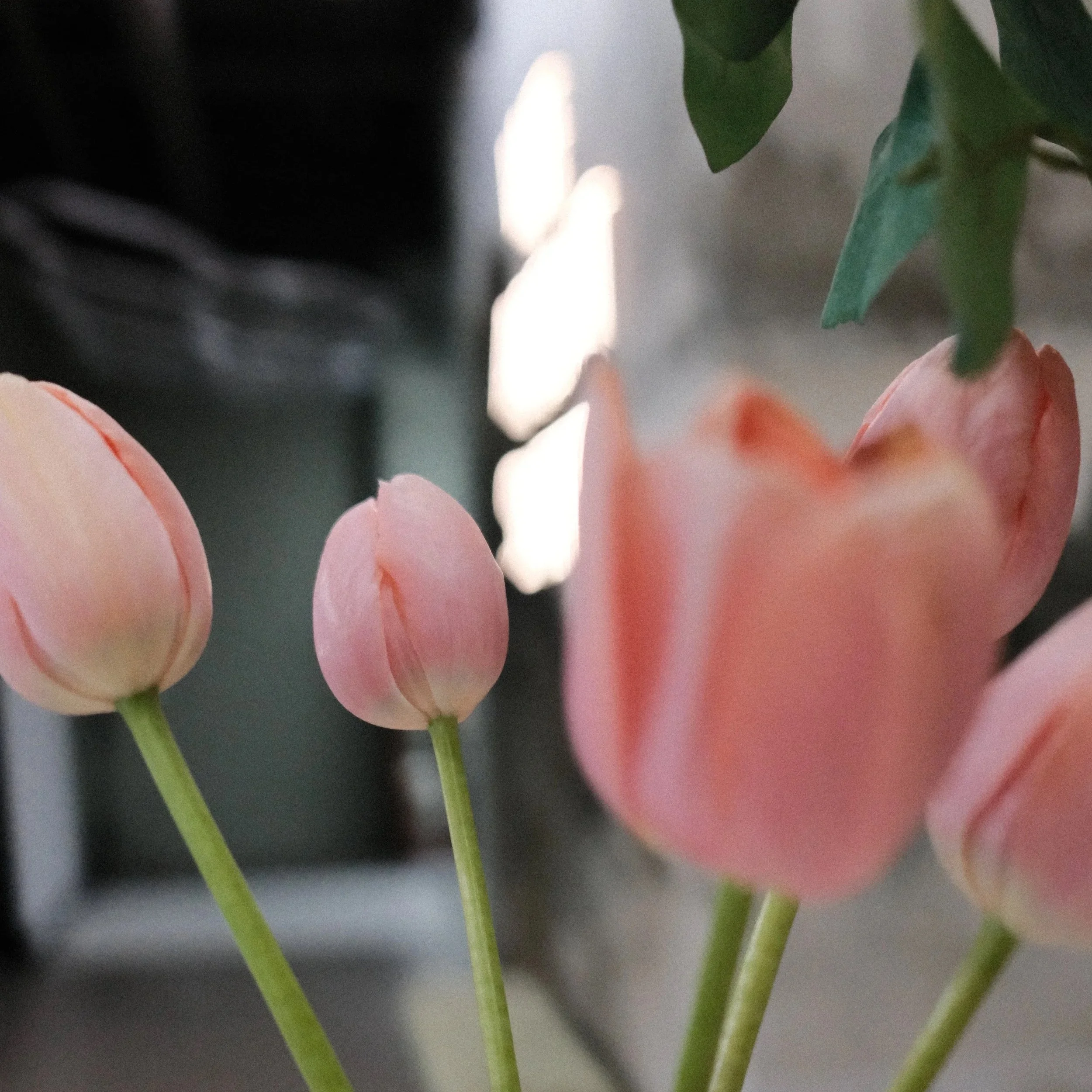 A close-up photograph of a floral arrangement with white and pink tulips at the Minneapolis tattoo studio - The Wolf Den Tattoo and a large neon sign behind it saying "We Aren't Sheep"