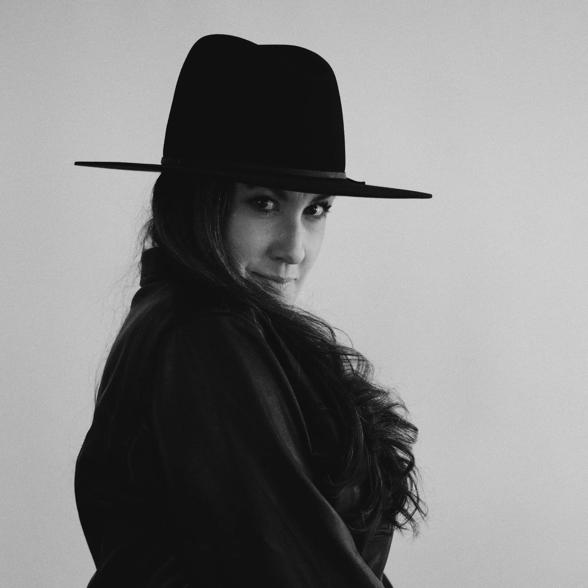 Black and white photo of a woman wearing a wide-brimmed hat, with long hair visible on one side, looking slightly to the side.