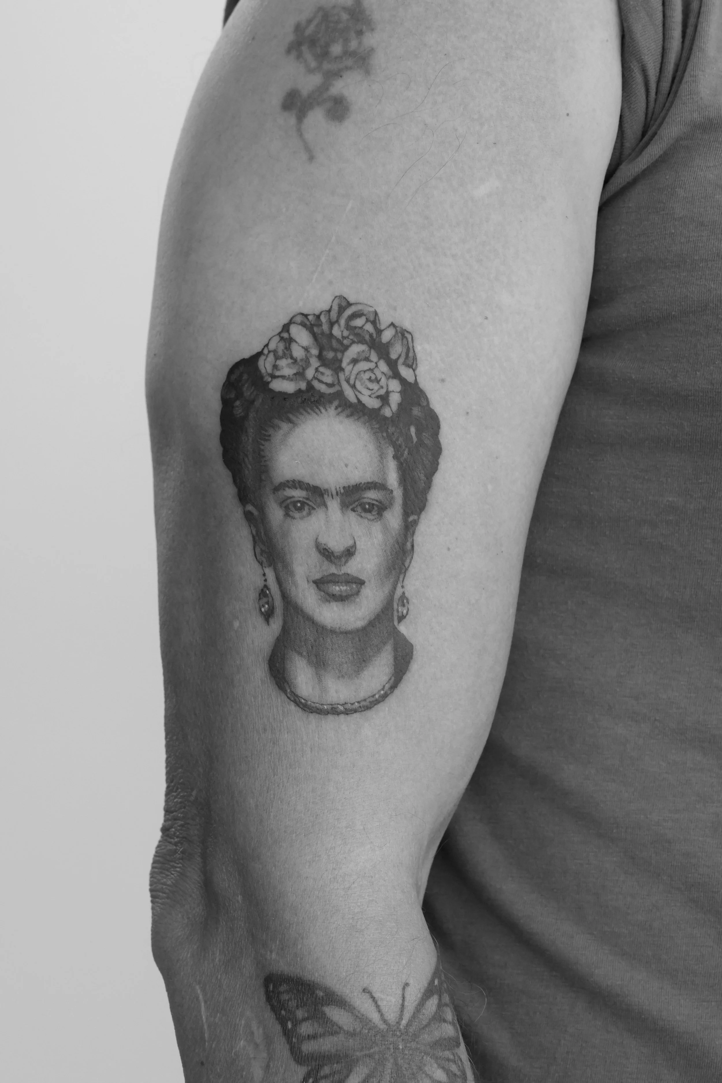 Black and white photo of a person's upper arm with multiple tattoos, including a portrait of a woman with flowers in her hair.