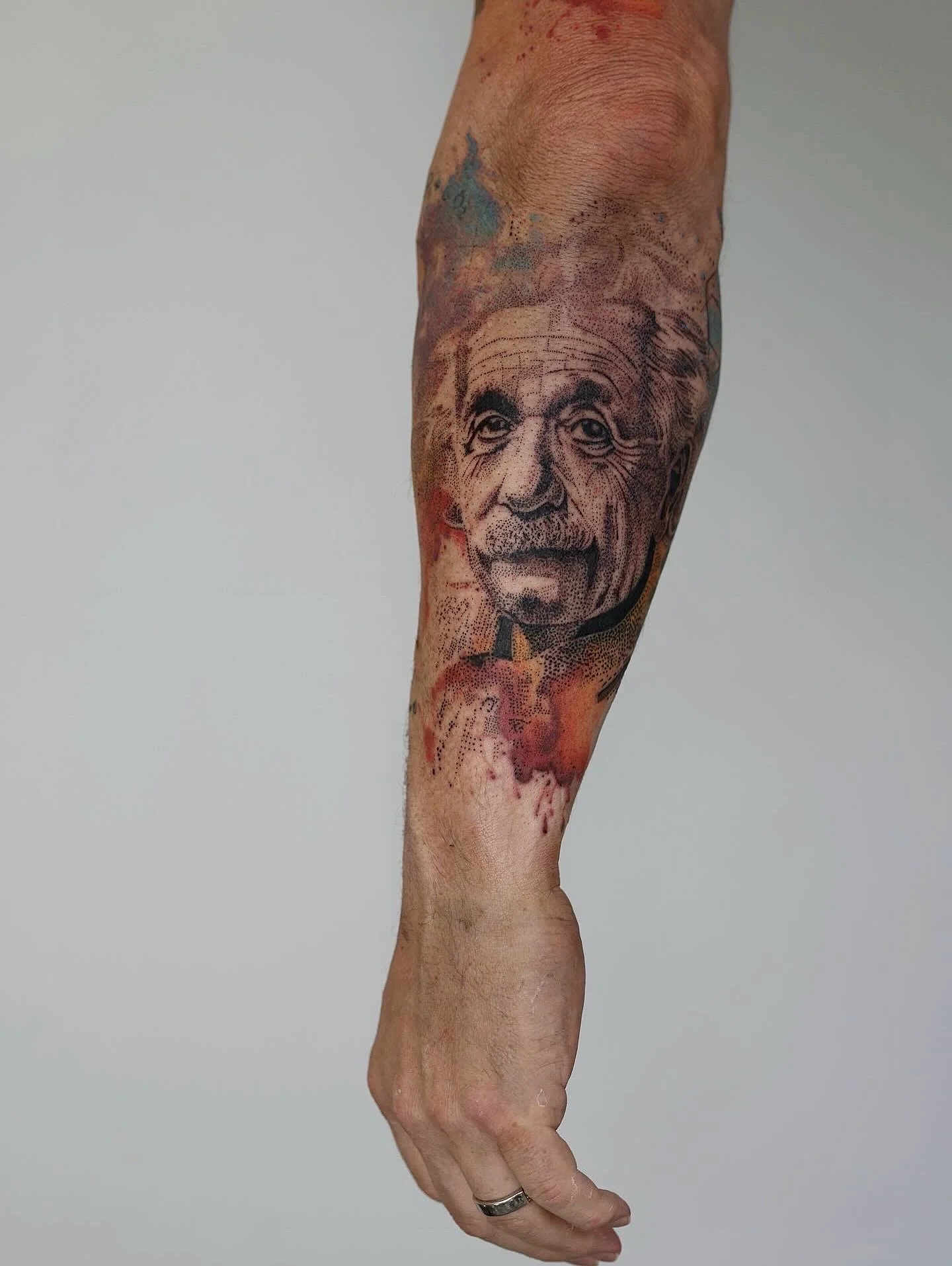 A pointillism portrait of Albert Einstein with a watercolor splashes behind him. This is a forearm tattoo
