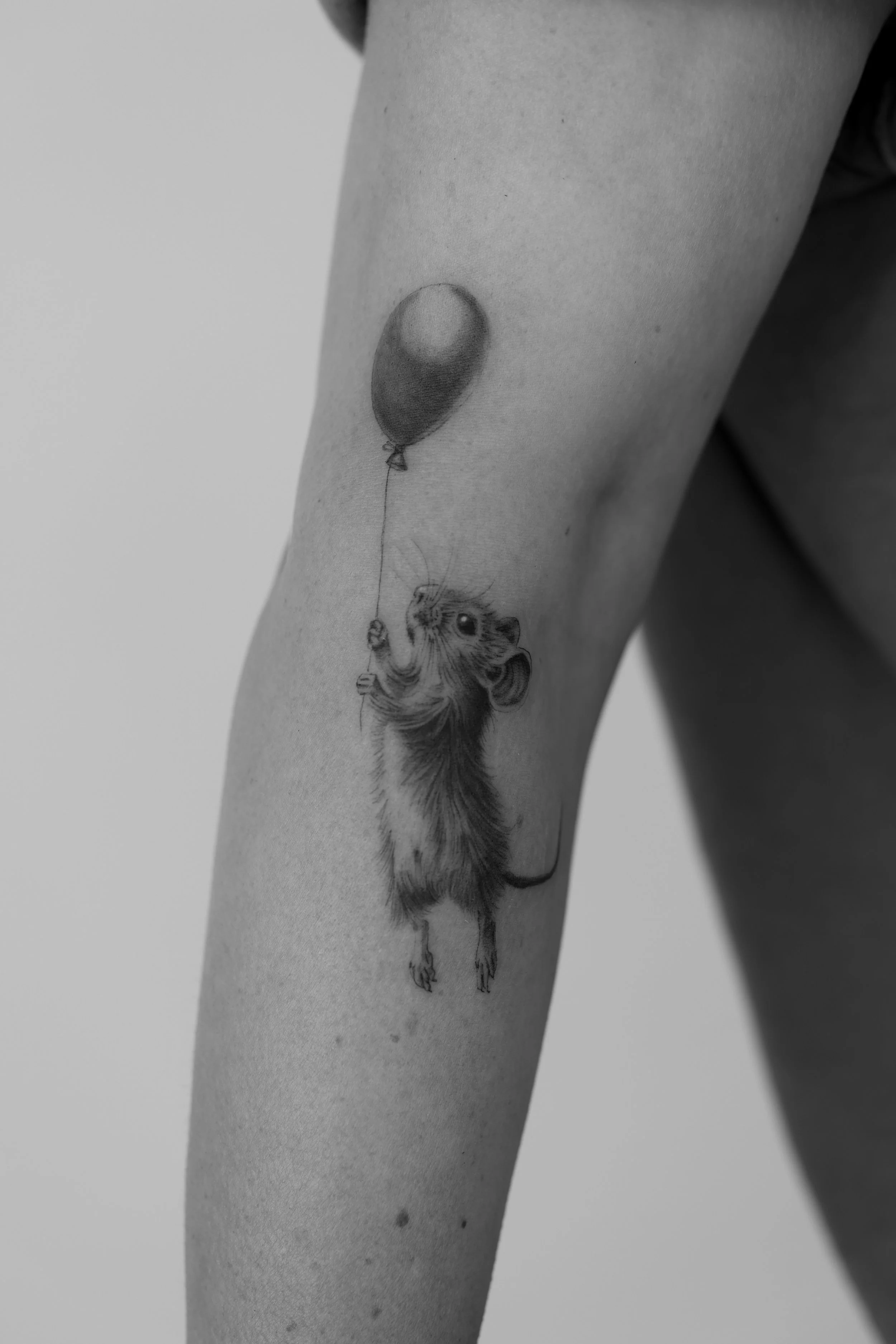 Tattoo of a mouse holding a balloon on a person's arm in black and white