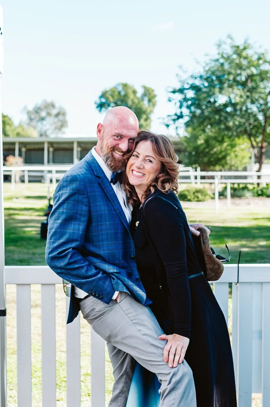 A couple happily posing outdoors on a sunny race day at the Walgett Races in Bill's Bunker, the best country race day in NSW.