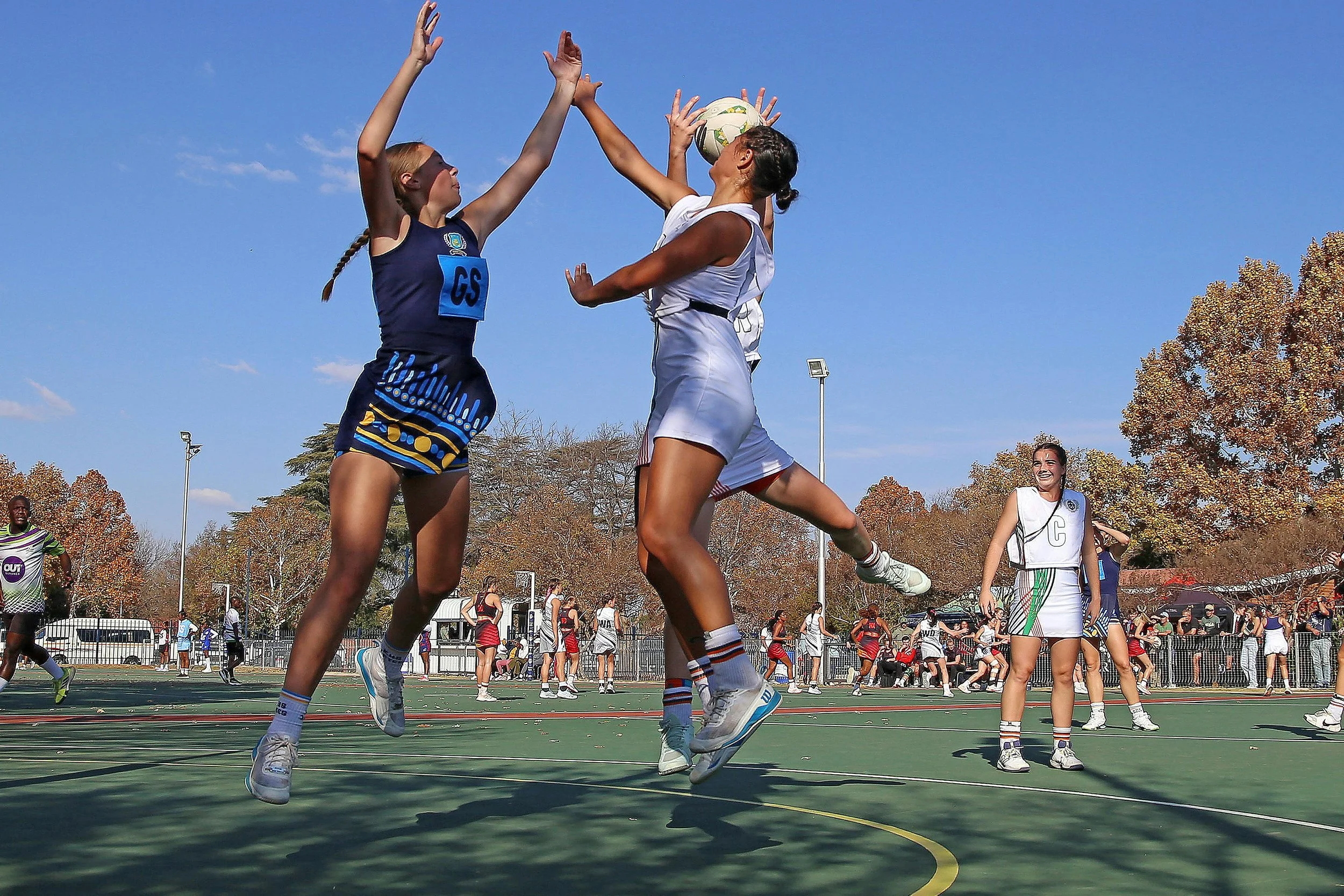 Three outdoor senior netball players jump to receive a pass