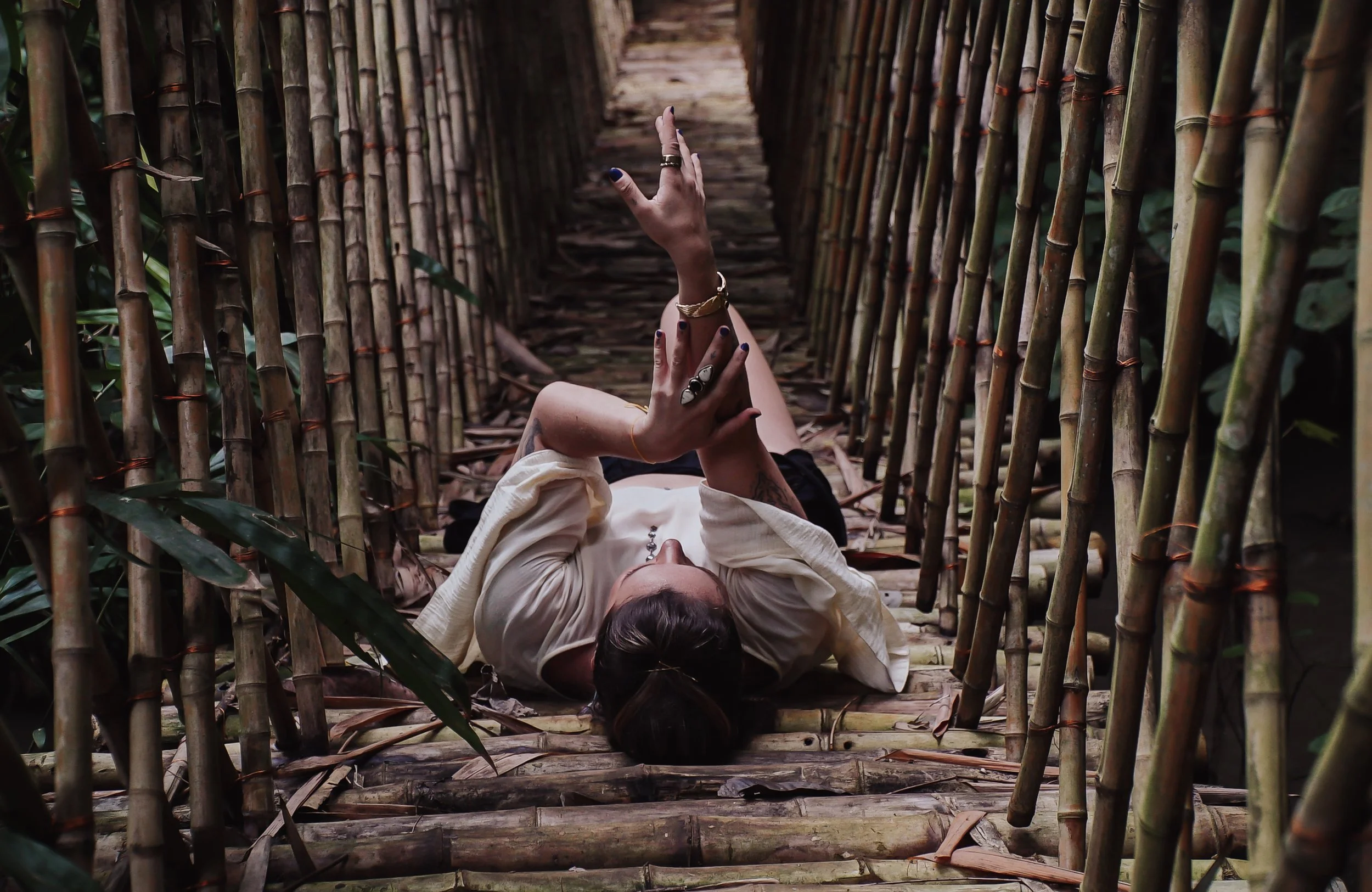 Person lying on bamboo walkway, holding phone, surrounded by bamboo stalks.
