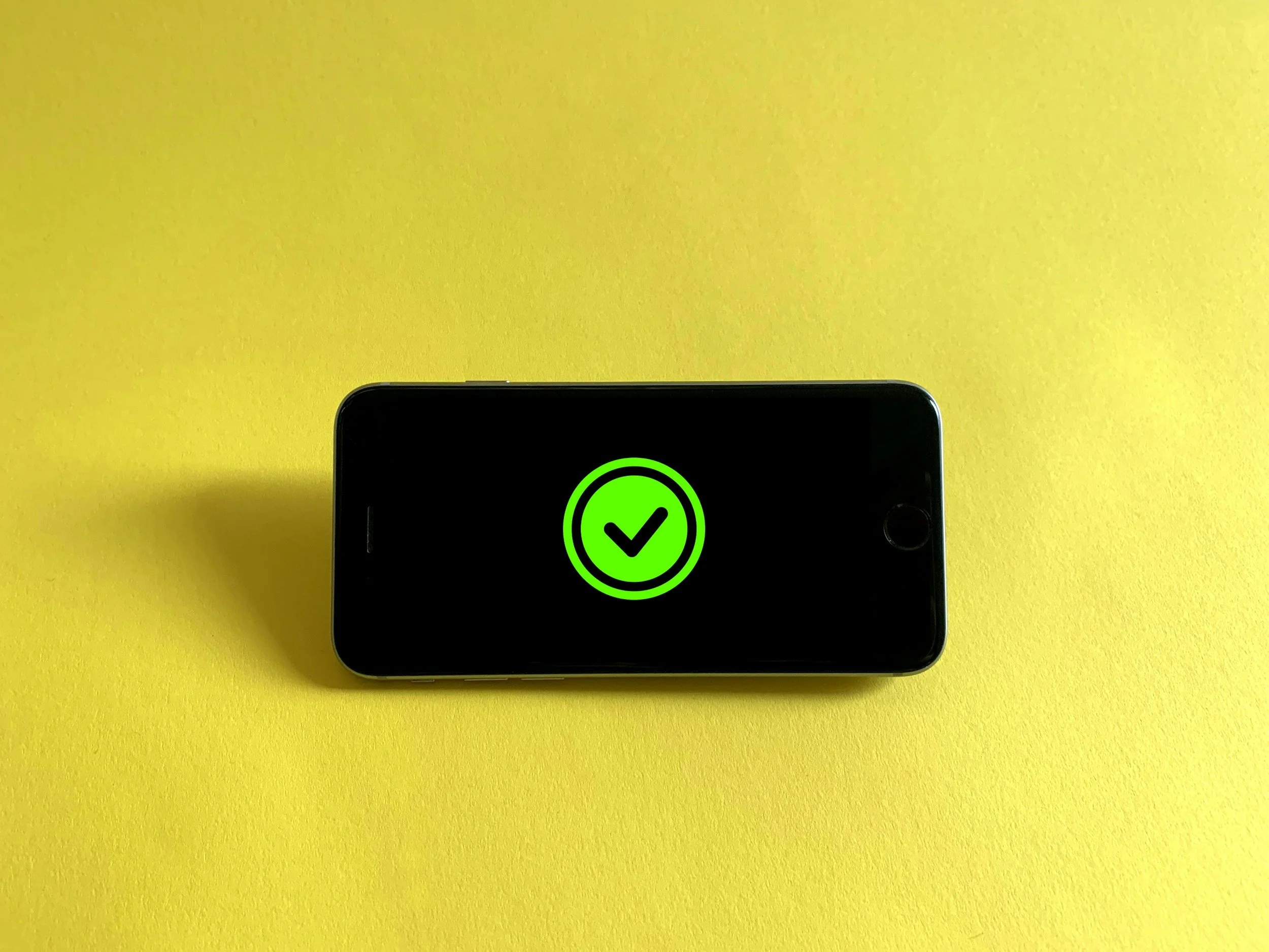 Close-up of a smartphone displaying a green checkmark on a black screen, resting on a yellow surface.