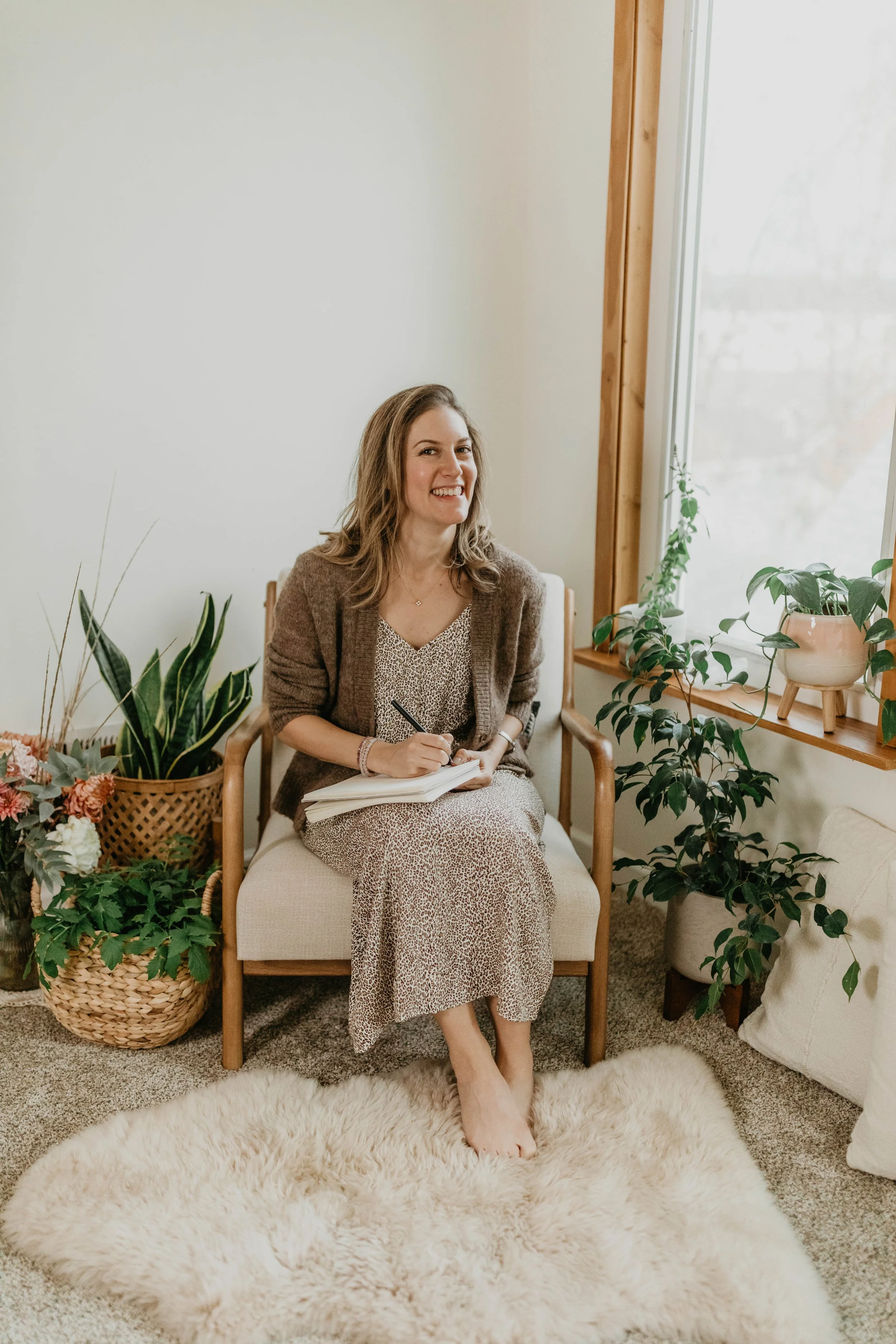 woman sitting in a chair, smiling at the camera, writing in her notebook