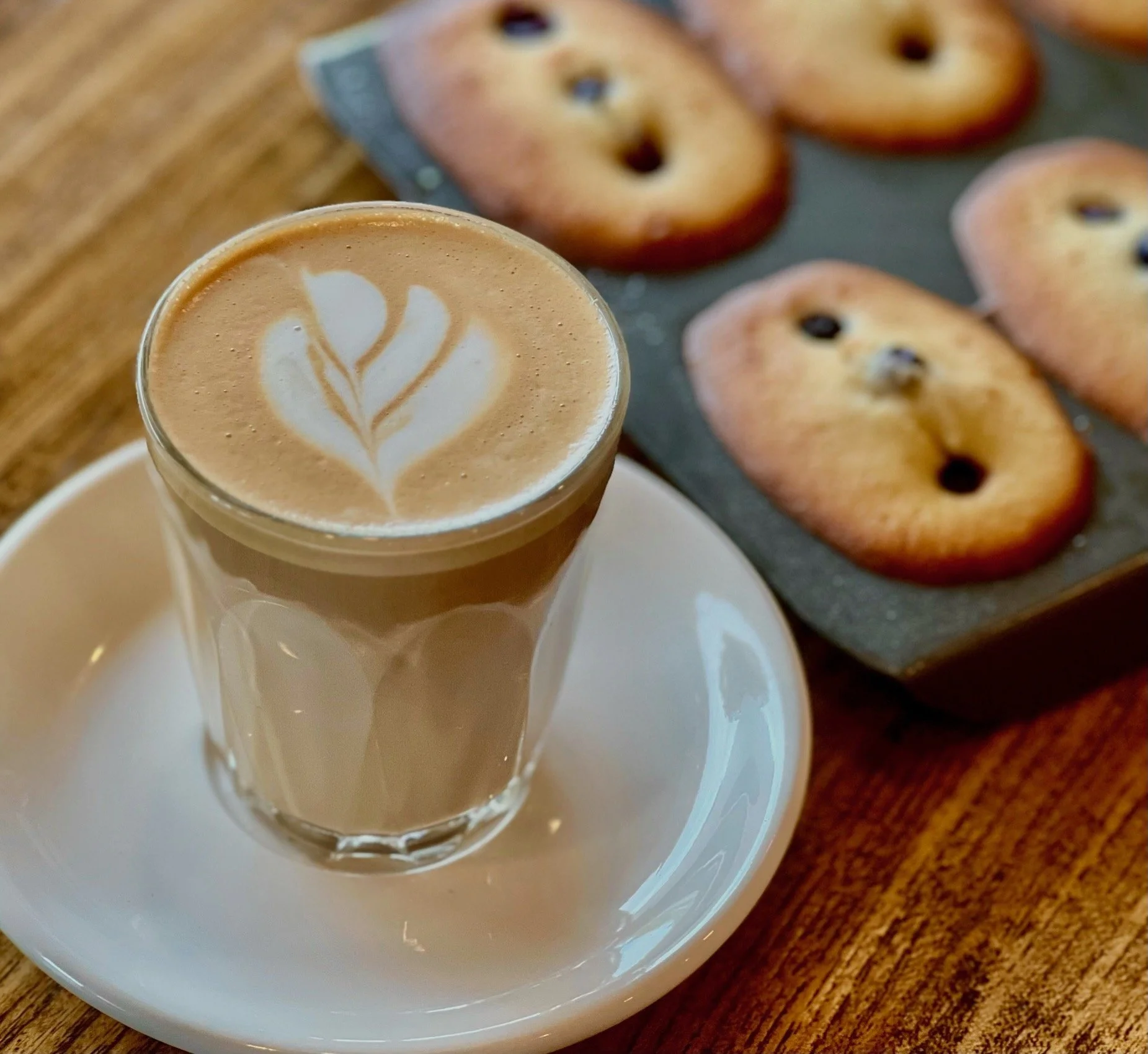 Freshly backed Gluten Free Raspberry Friands, still in their baking tray accompanied with a latte coffee.