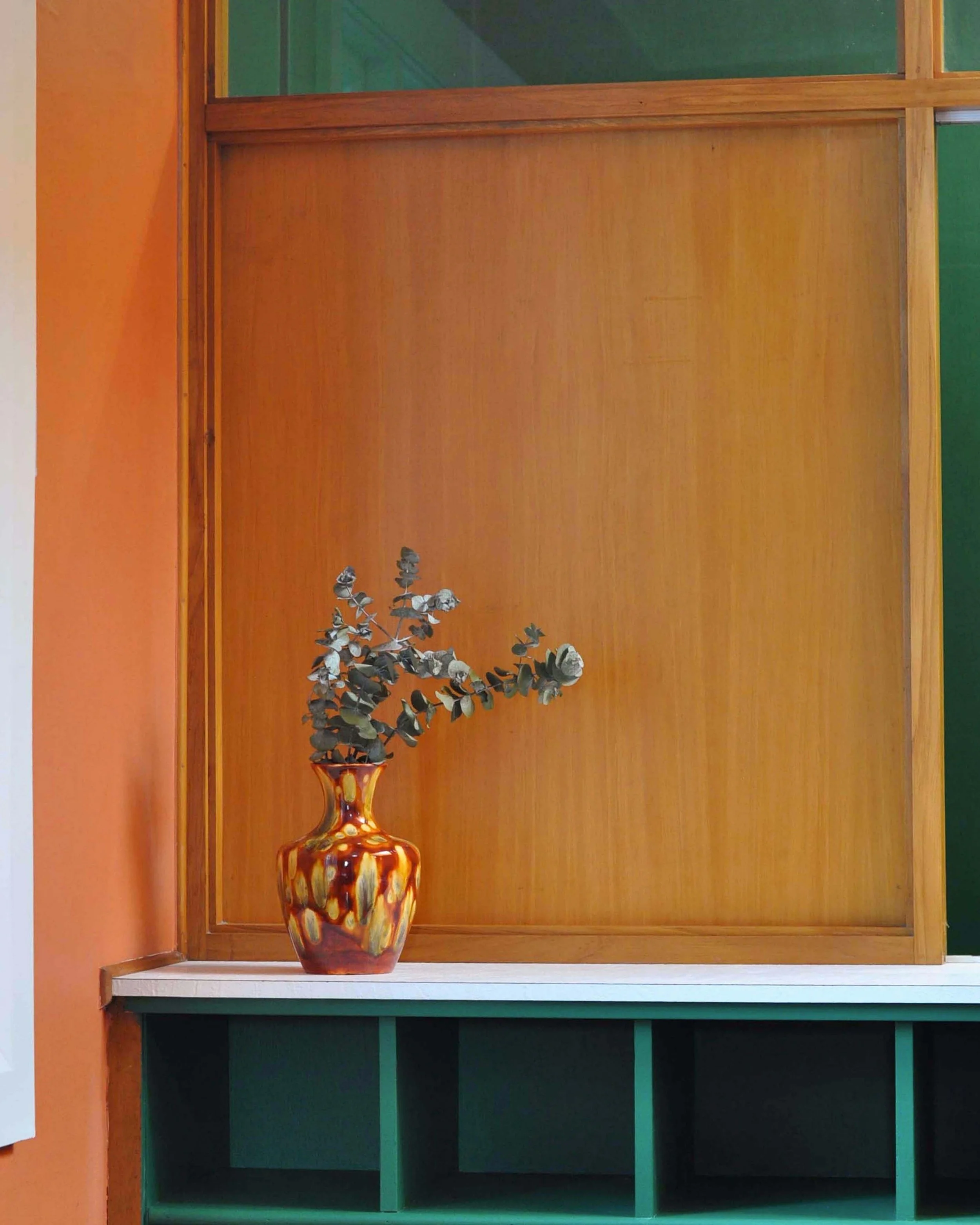A decorative vase with dried eucalyptus branches inside it, placed on a white shelf against a wooden wall.