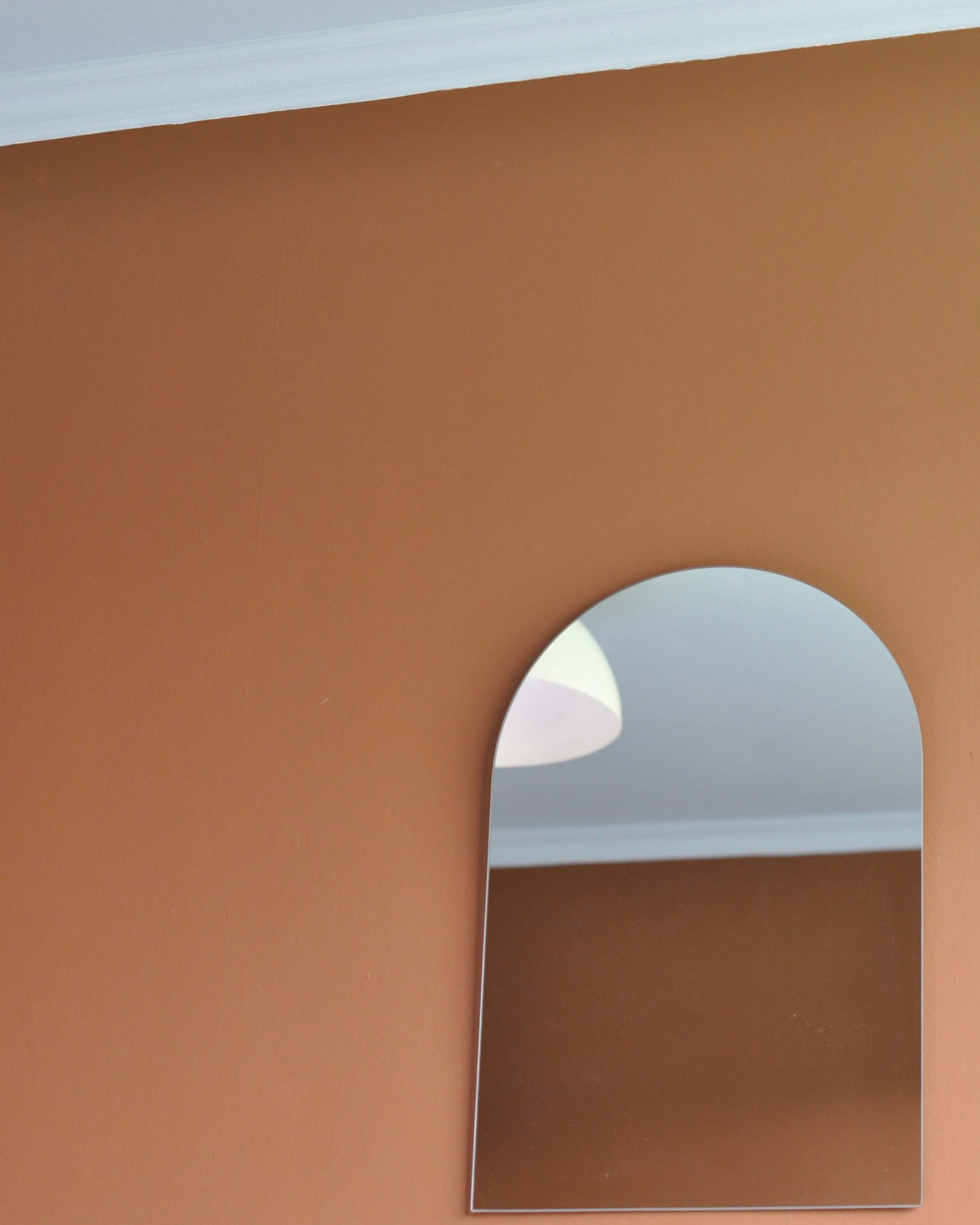 Close-up of two mirrors on a brown wall, showing reflections of the ceiling with white trim and a white door frame.