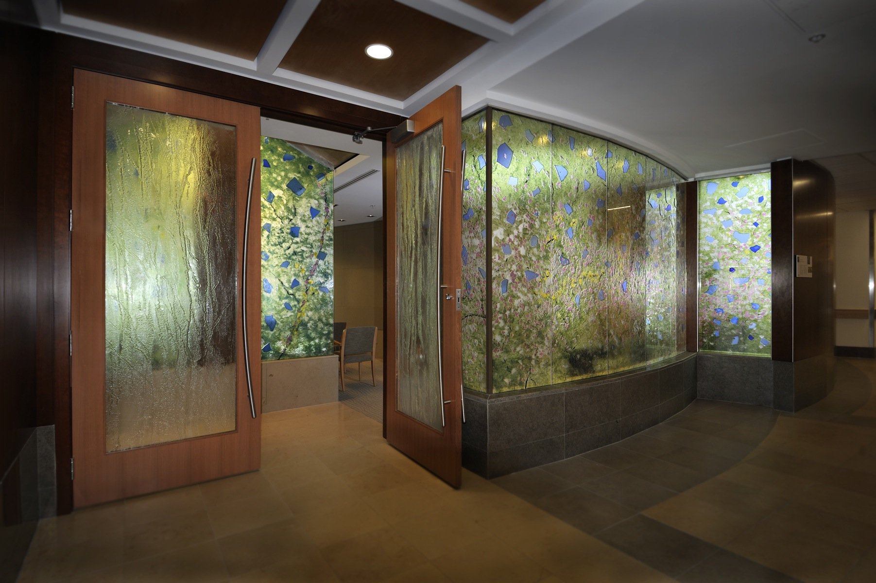 Interior view of a hallway with wooden doors with textured glass, leading to a room with colorful leaf-themed wall art and green canopy paintings.