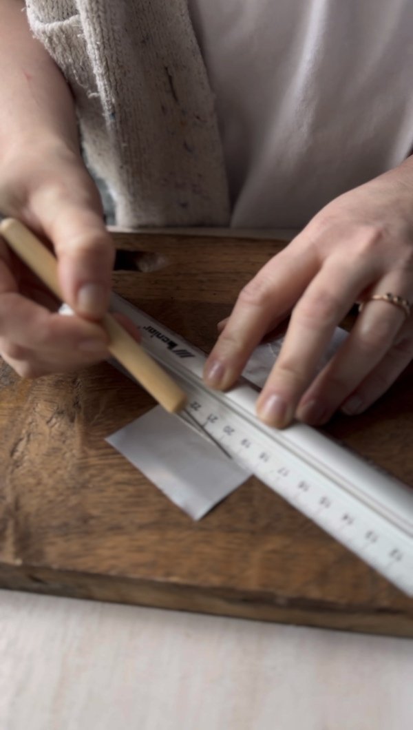 Using a ruler and pen to mark fold lines on a rectangular aluminum piece.