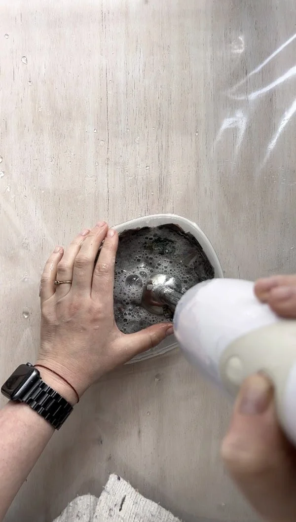 Hand-held blender being used to blend soaked newspaper pieces into pulp for a DIY handmade paper project.