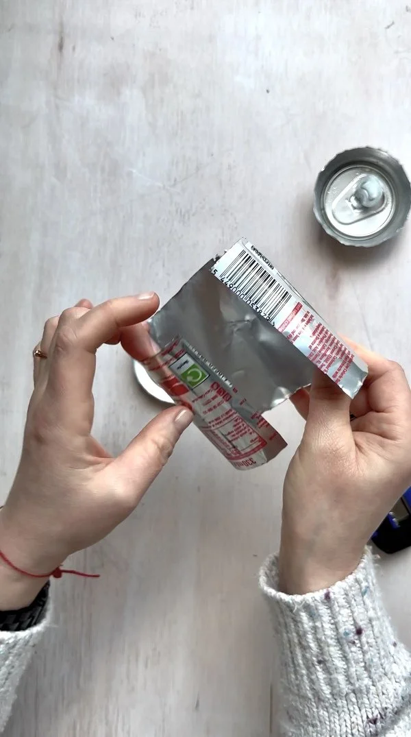 Flattening a cut aluminum can sheet by pulling it along the edge of a
