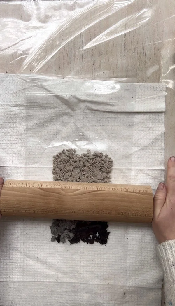 Gently rolling out the paper pulp with a rolling pin, using cellophane and a cloth to press and flatten the layers in the papermaking process.