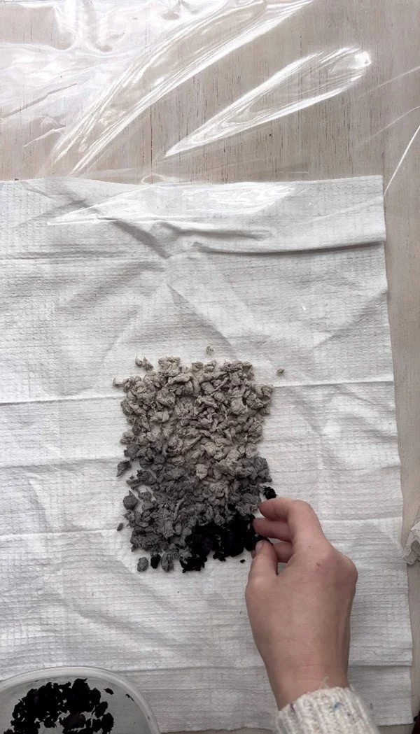 Arranging various shades of recycled paper pulp from light gray to black on a cloth, preparing the design for the next steps in the handmade papermaking process.