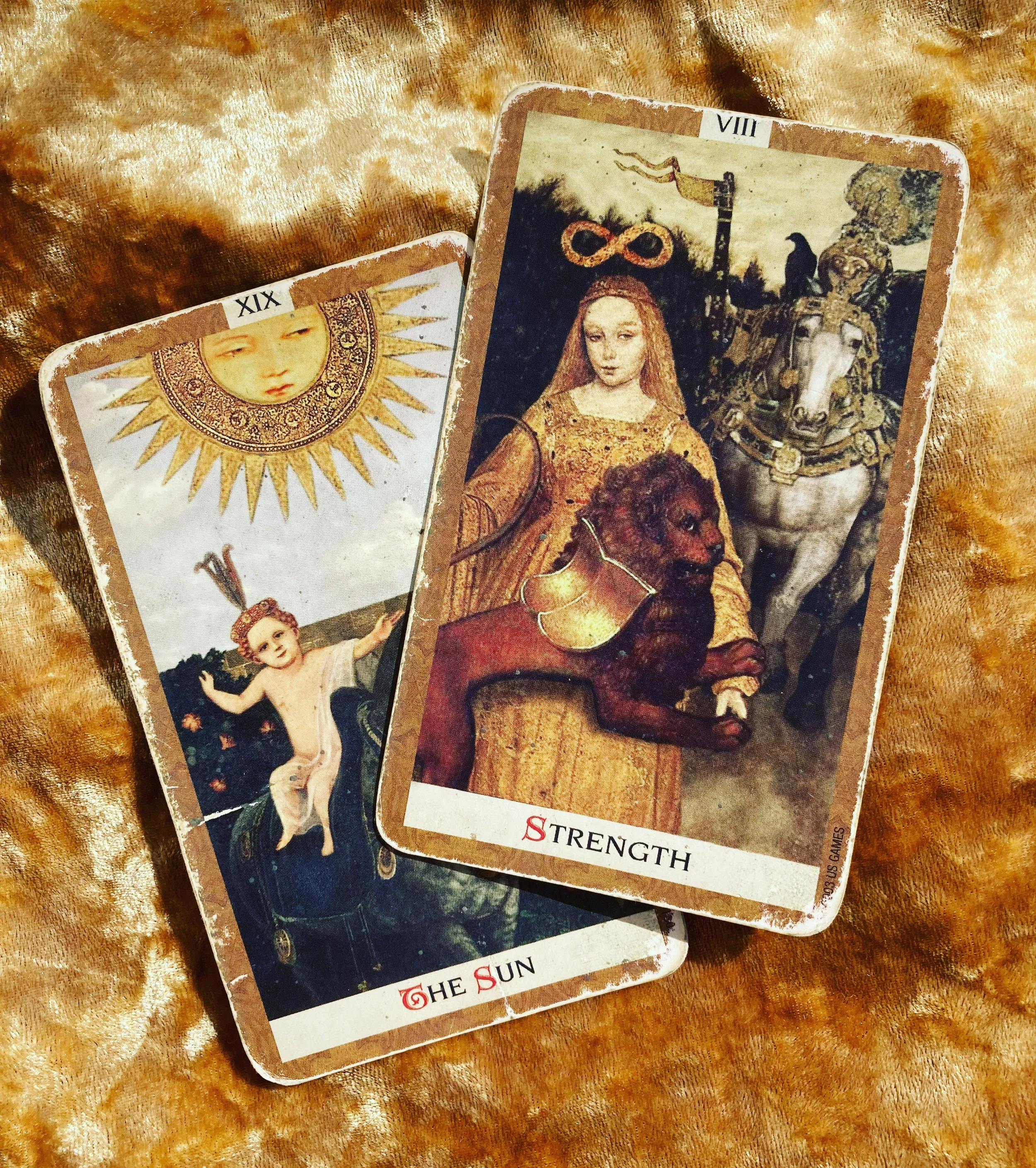 To tarotkort, "The Sun" og "Strength", på en gylden bakgrunn.