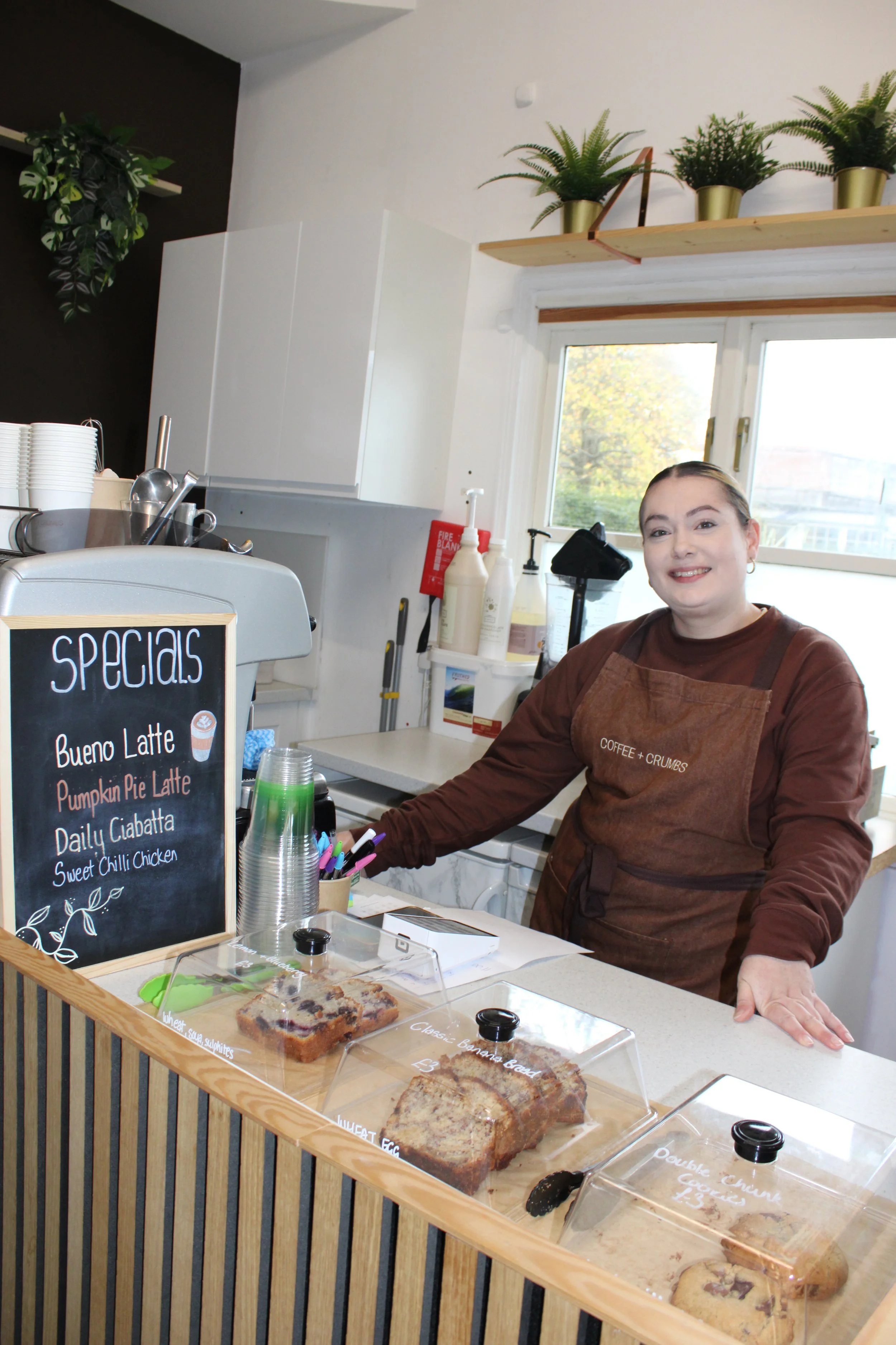 smiling woman, stood in coffee shop, with baked goods