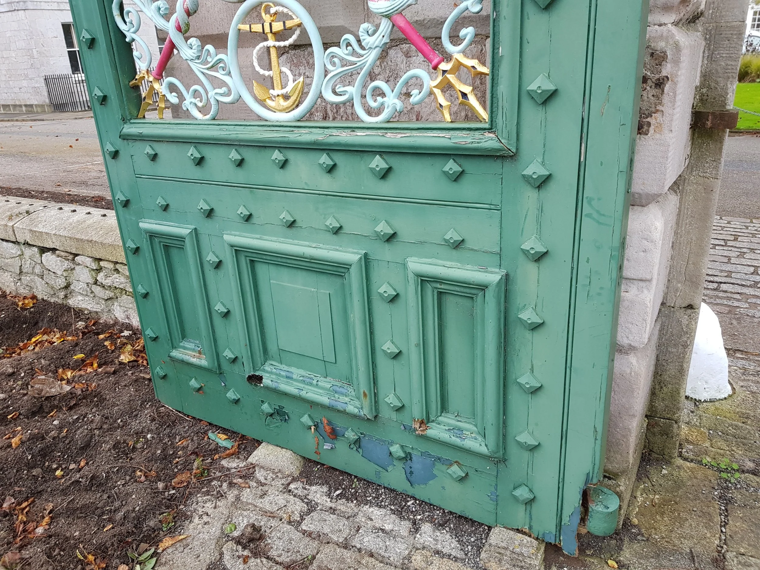 A decorative green gate with metal studs and an ornate design, featuring a painted anchor symbol behind the gate.