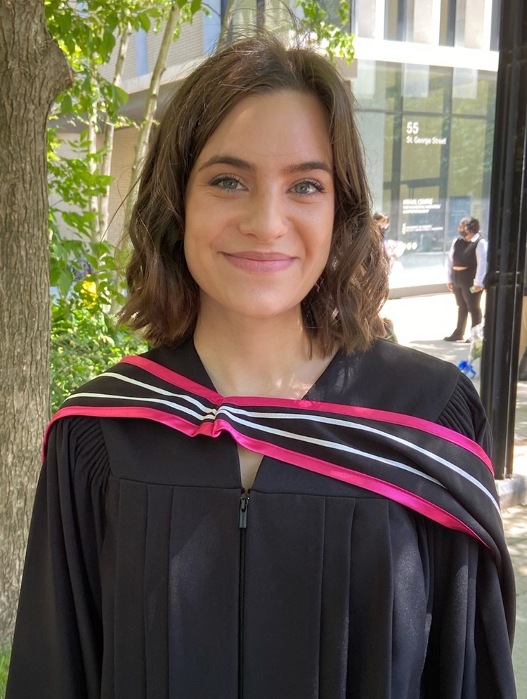 Victoria smiles at the camera while wearing a black graduation gown and red striped graduation sash.
