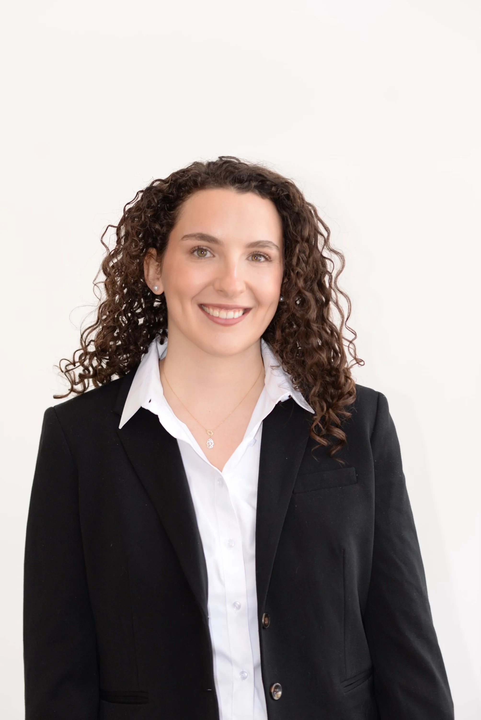 Yardena Gerwin smiles at the camera while wearing a white blouse and black blazer. She is a white woman with curly brown hair.