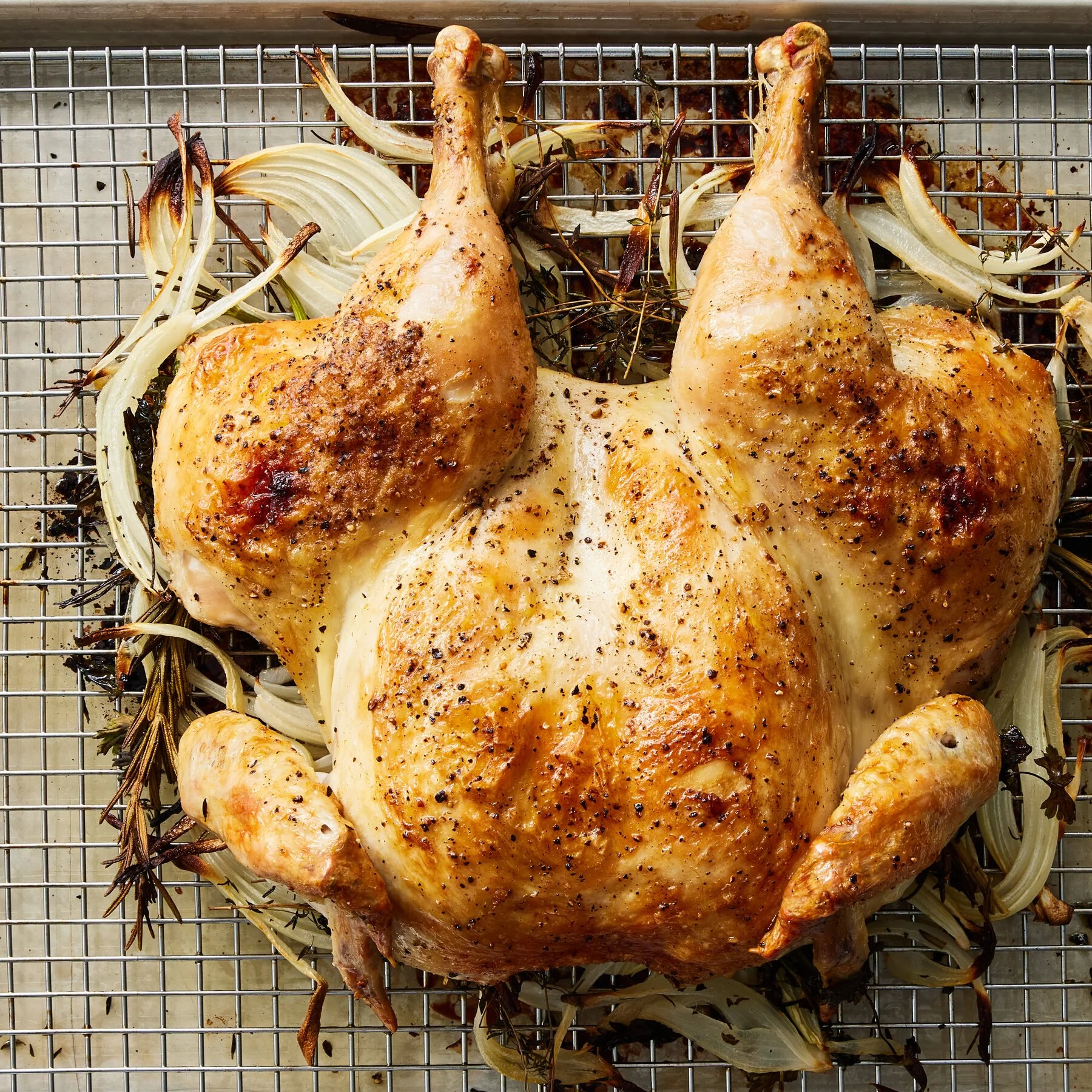 A whole roasted chicken on a wire rack over sliced onions and herbs