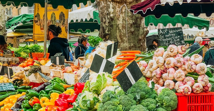 Outdoor market stall piled with peppers, broccoli, carrots and garlic under green awnings
