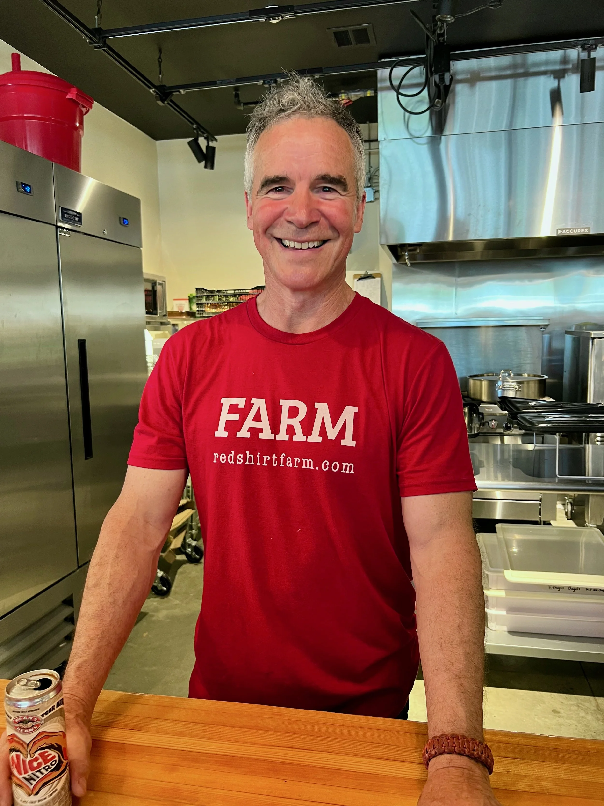 A smiling man in a red FARM t-shirt standing in the farm store kitchen