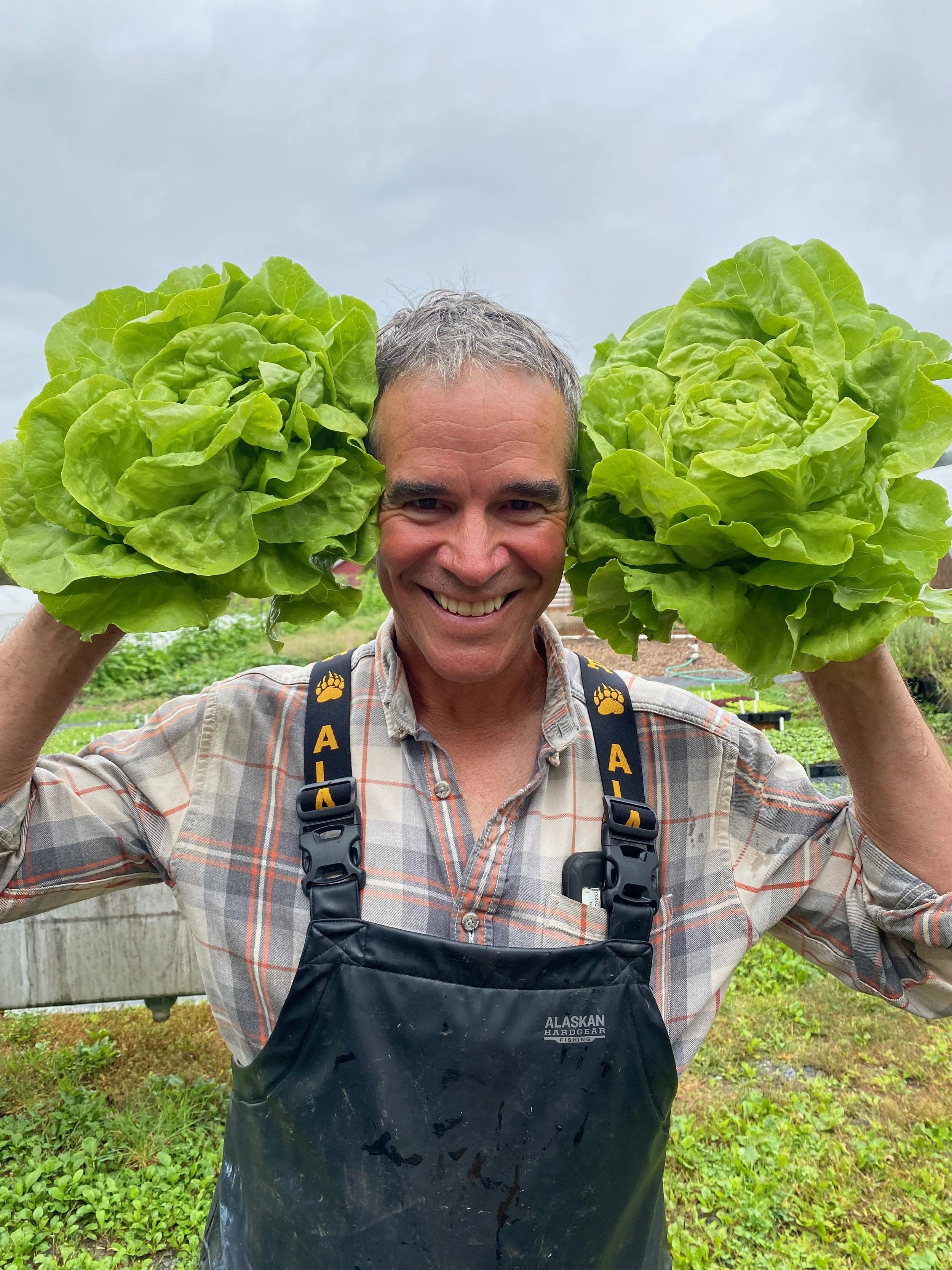 A man in overalls holding two heads of lettuce