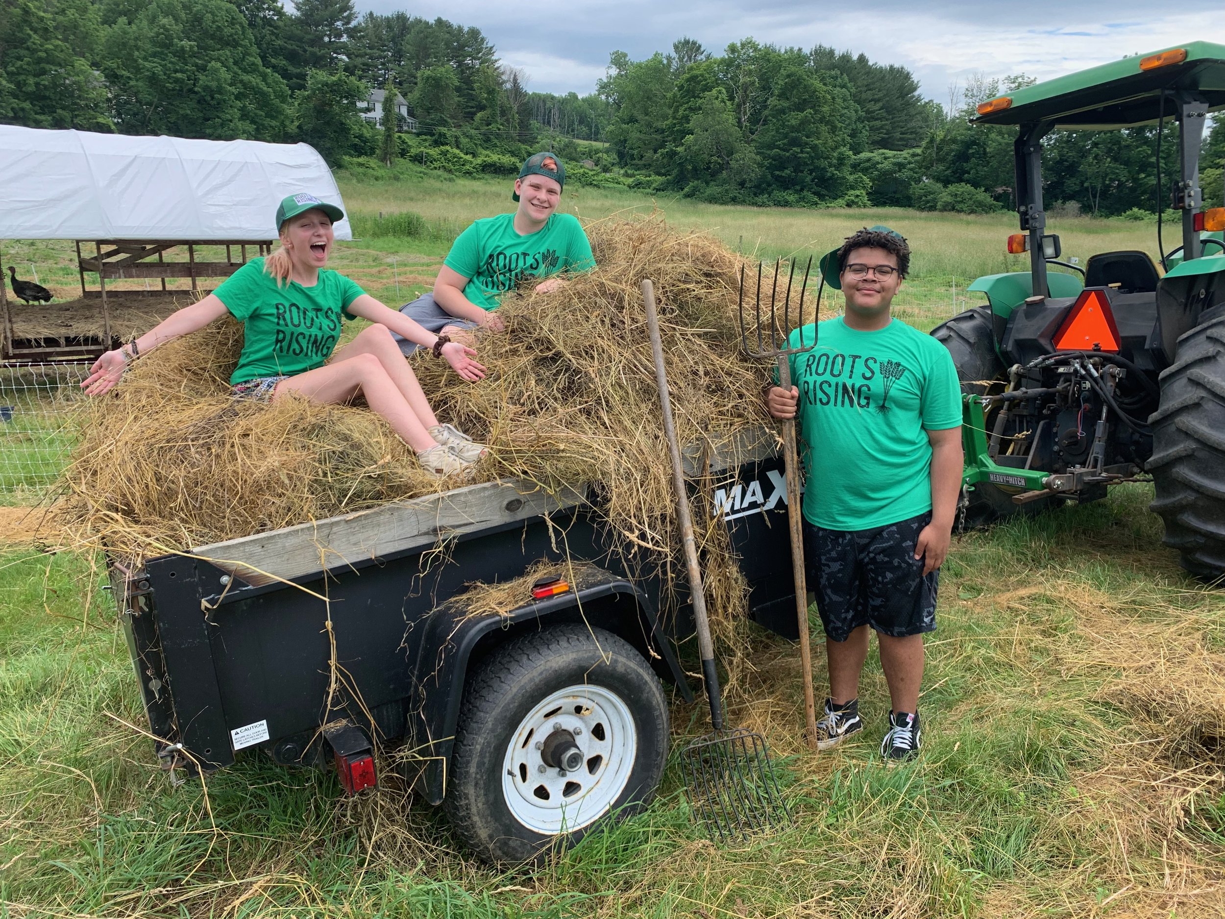 Three Roots Rising students in green shirts on a cart of hay beside a tractor