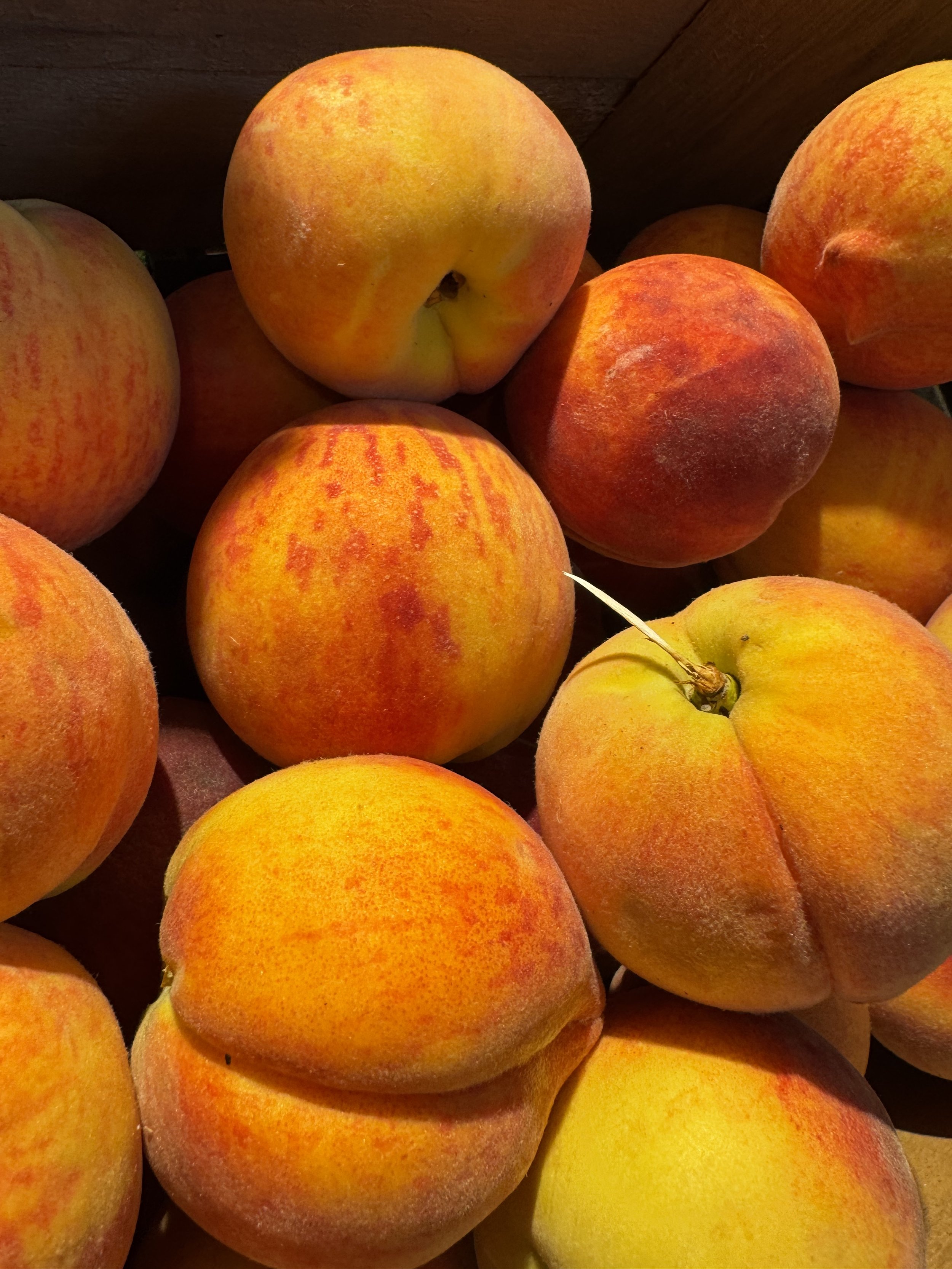 A crate of ripe peaches with red blush on yellow skin