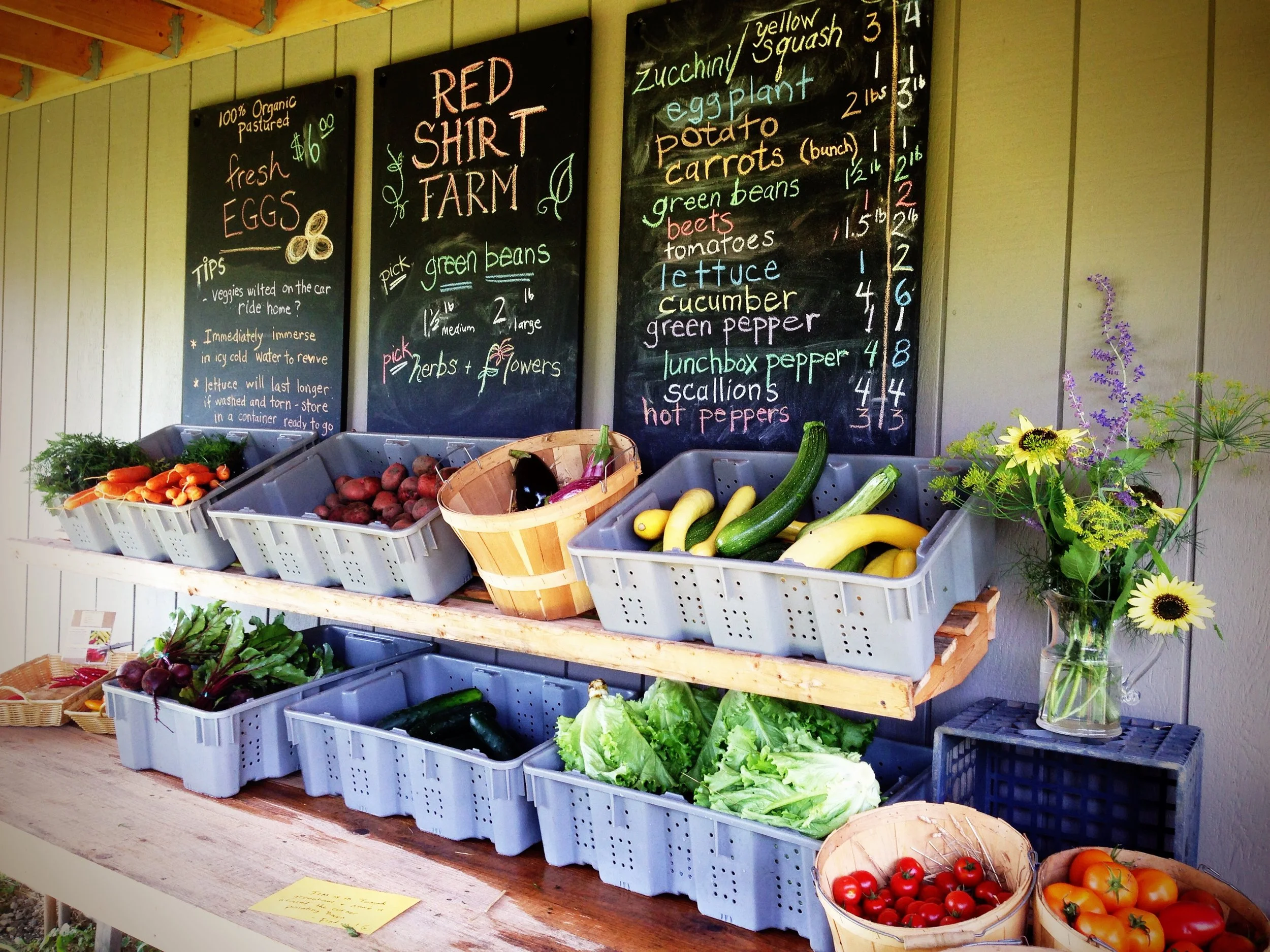 The Red Shirt Farm stand with chalkboard price signs and baskets of fresh produce