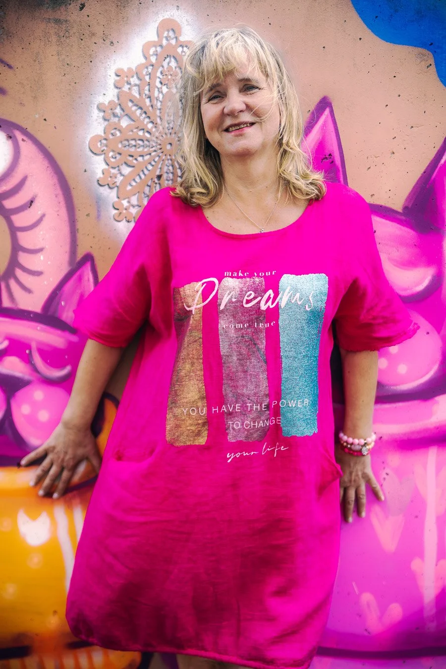 Portret lifestyle wykonany na Wilanowie, fotografia Konrad Uhma — uśmiechnięta poza na tle graffiti w intensywnych barwach, mural z kocimi sylwetkami i abstrakcyjnymi wzorami tworzy energetyczną oprawę