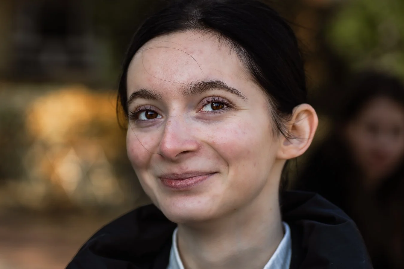 Lifestyle’owy portret wykonany w plenerze na terenie Ursynowa, zdjęcie twórca Konrad Uhma — fotografia z naturalnym światłem, subtelny uśmiech, miękkie tło, ujęcie z bliska