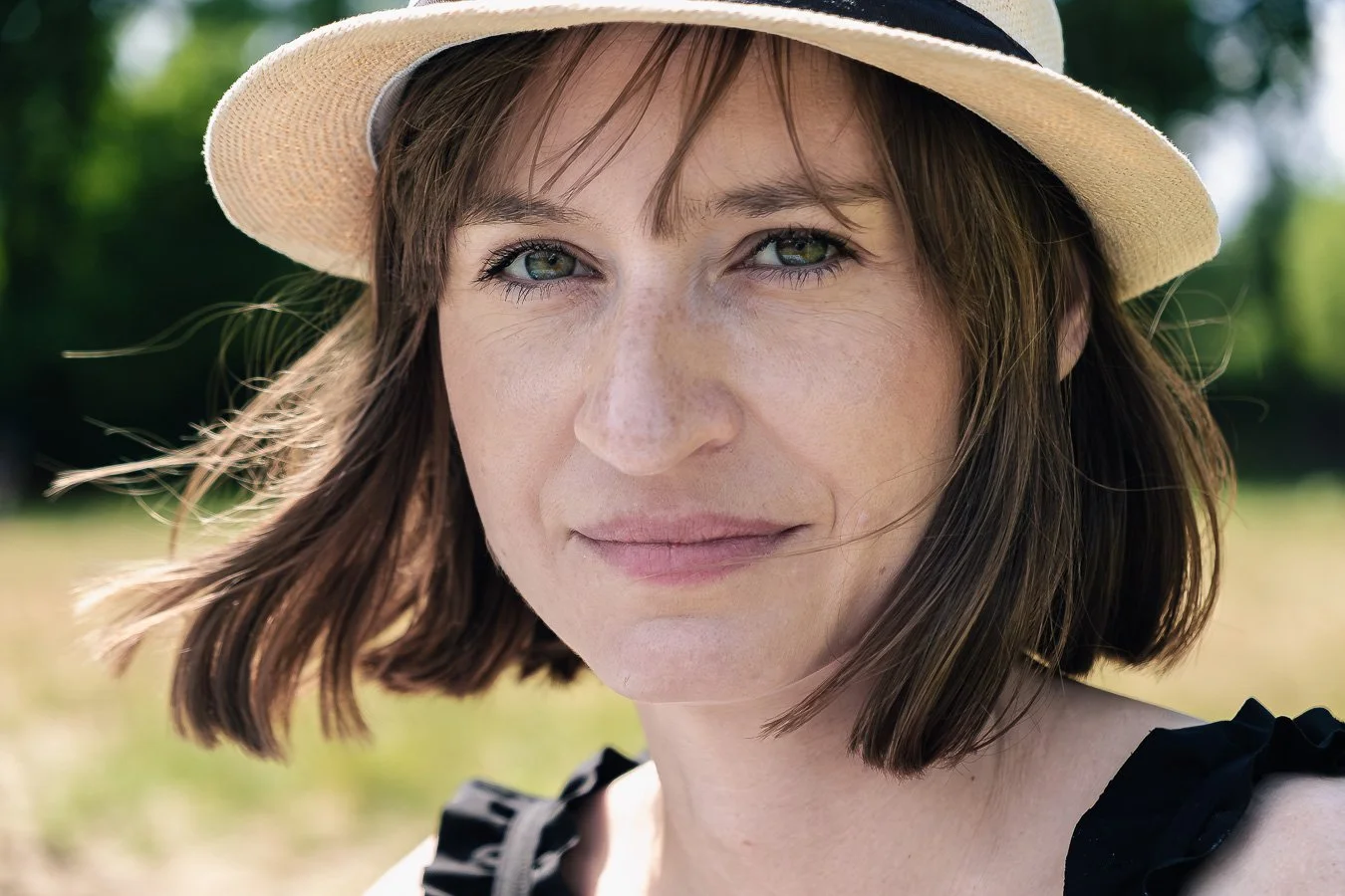 Portret lifestyle wykonany w plenerze na terenie Powsina, naturalne światło, twórca Konrad Uhma — zdjęcie kobiety w kapeluszu, fotografia z miękkim tłem i wyraźnym światłem dziennym
