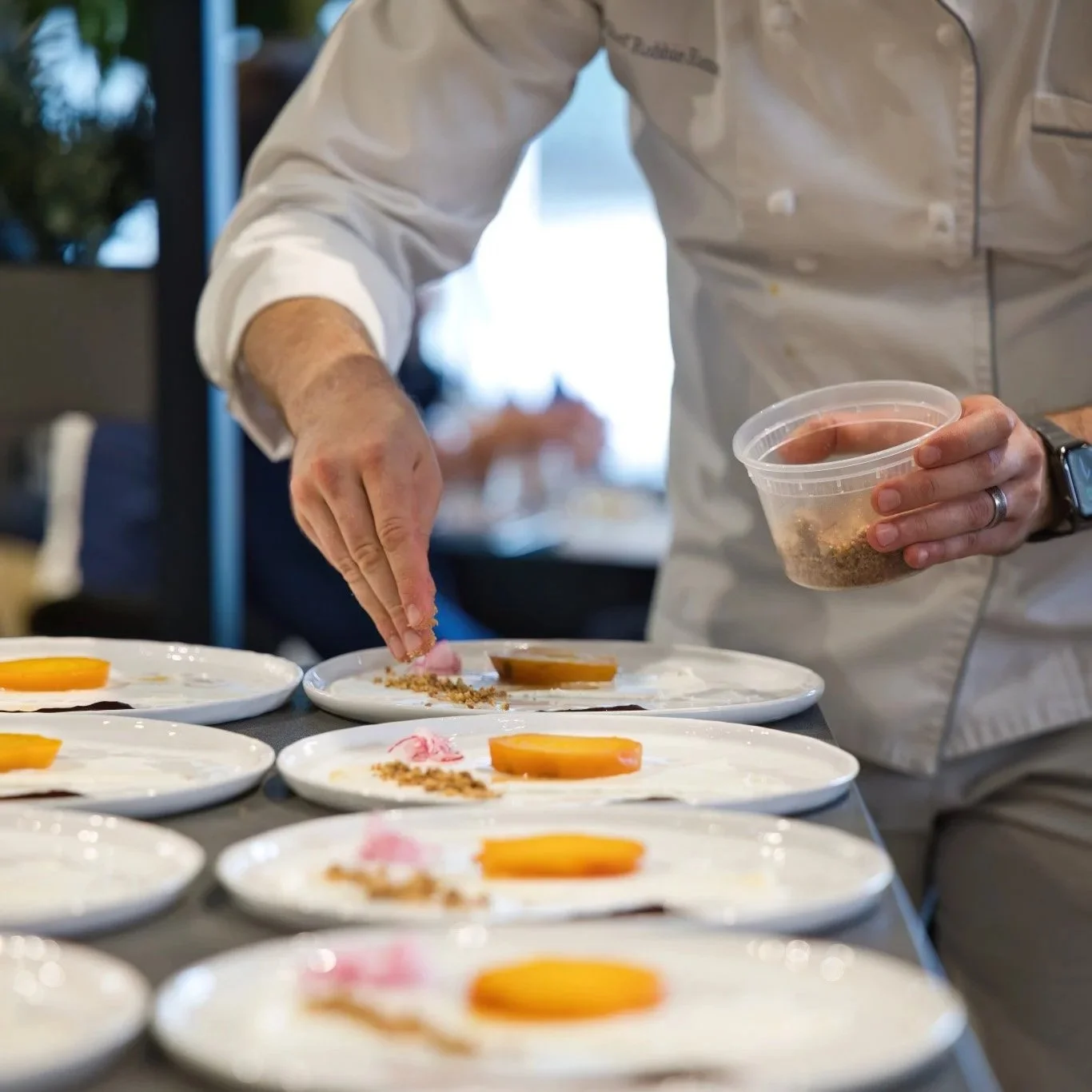 Chef preparing plates with sliced fruit and toppings in a professional kitchen.