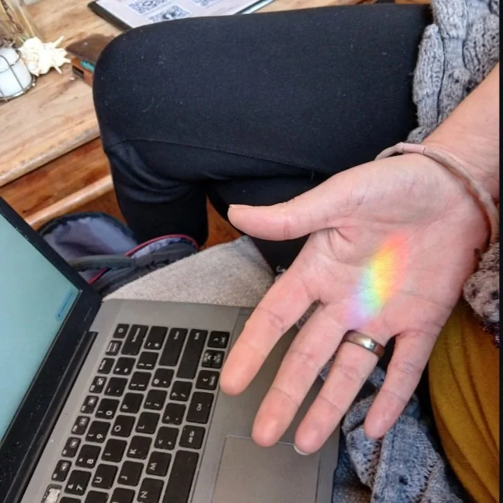 A person sitting on a couch with a laptop, showing a rainbow reflection on their hand.