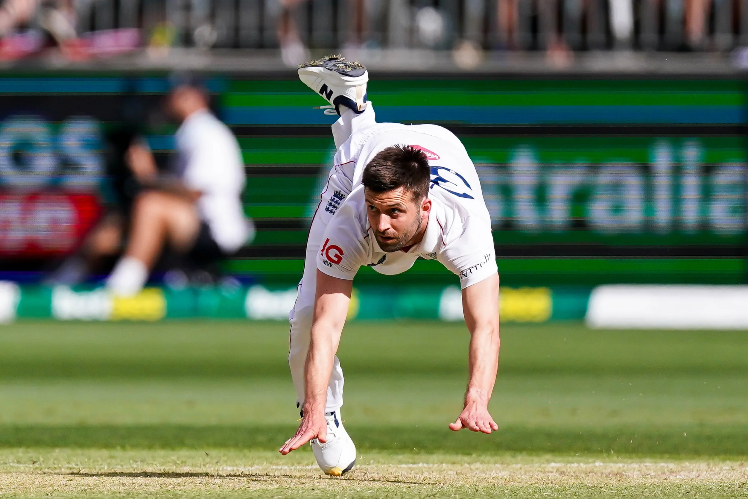 A cricket player in white uniform performing a handstand on the field during a match.