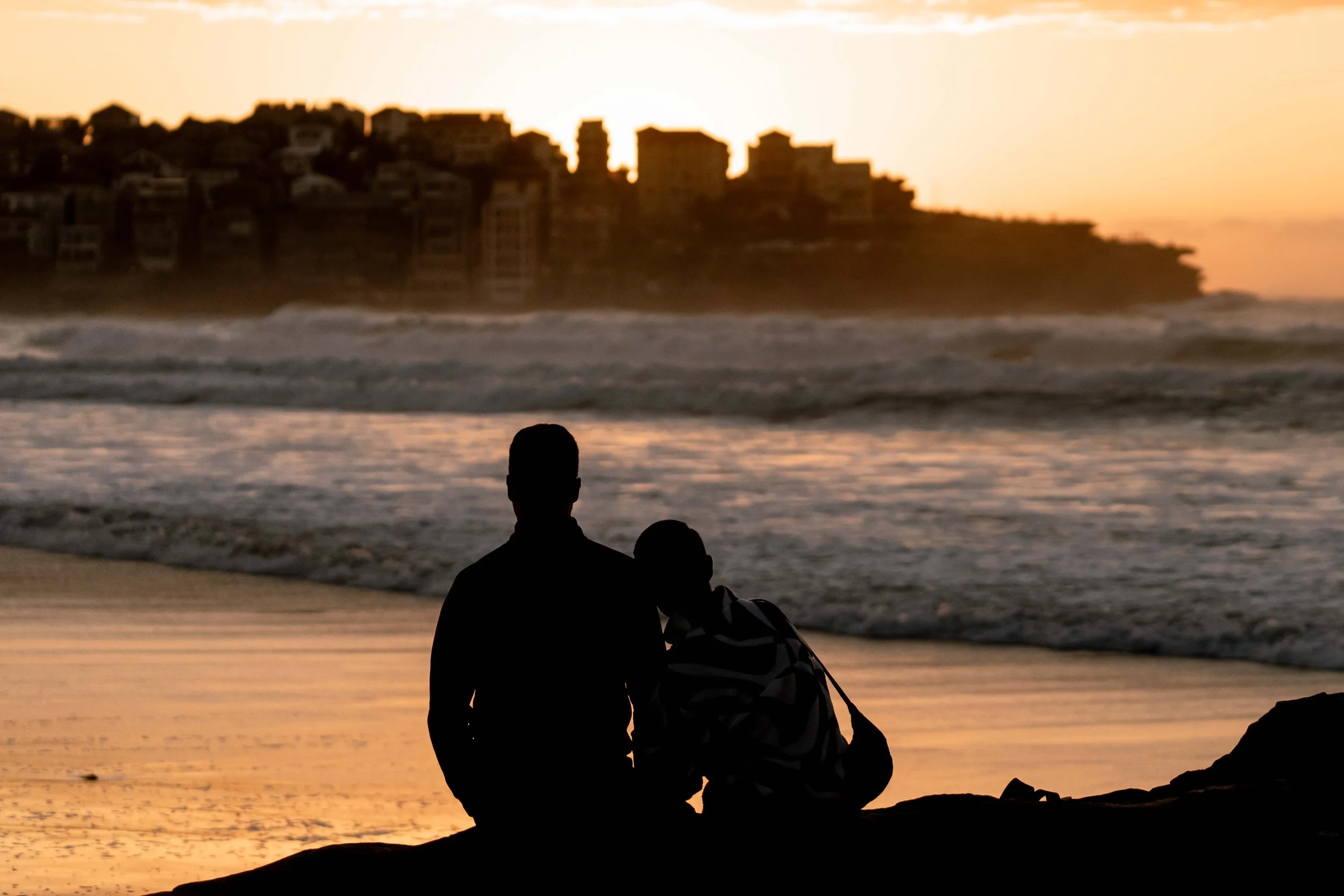 A couple sitting on rocks to watch the sunrise at Bondi Beach, Sydney, NSW, Australia