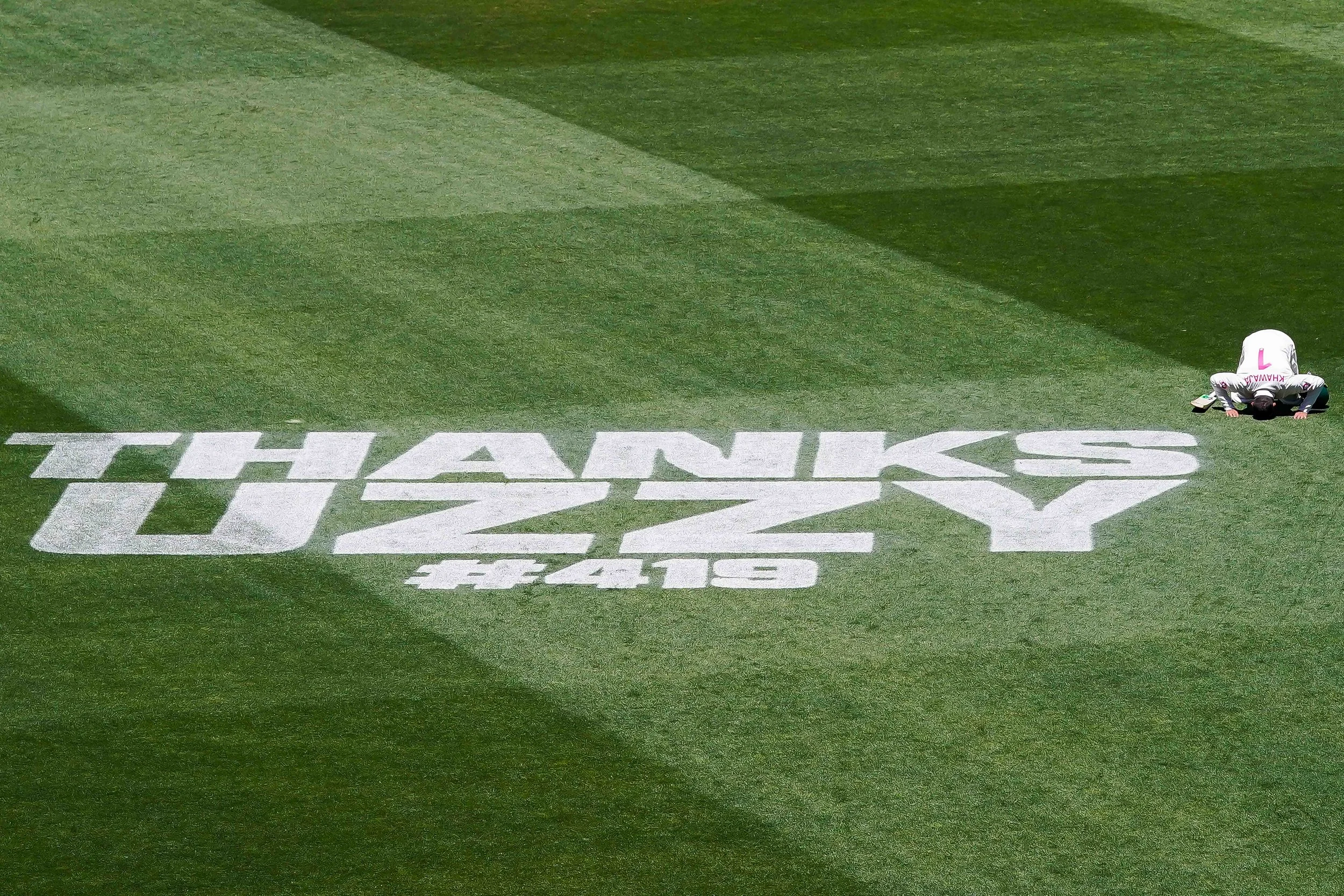 Usman Khwaja of Australia kisses the ground, in white placing the words "THANKS UZZY #419" painted on a grassy field.