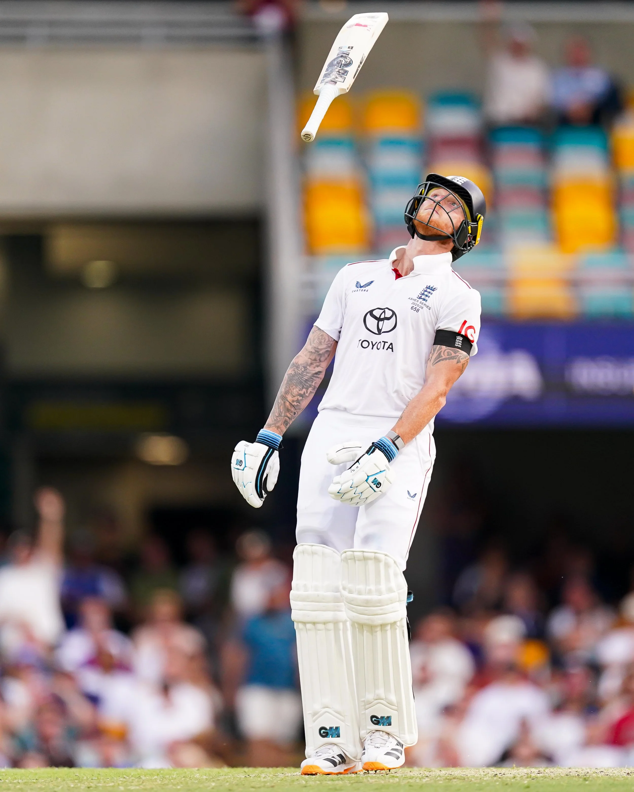 Cricket player throwing a cricket bat in a stadium with people in the background.