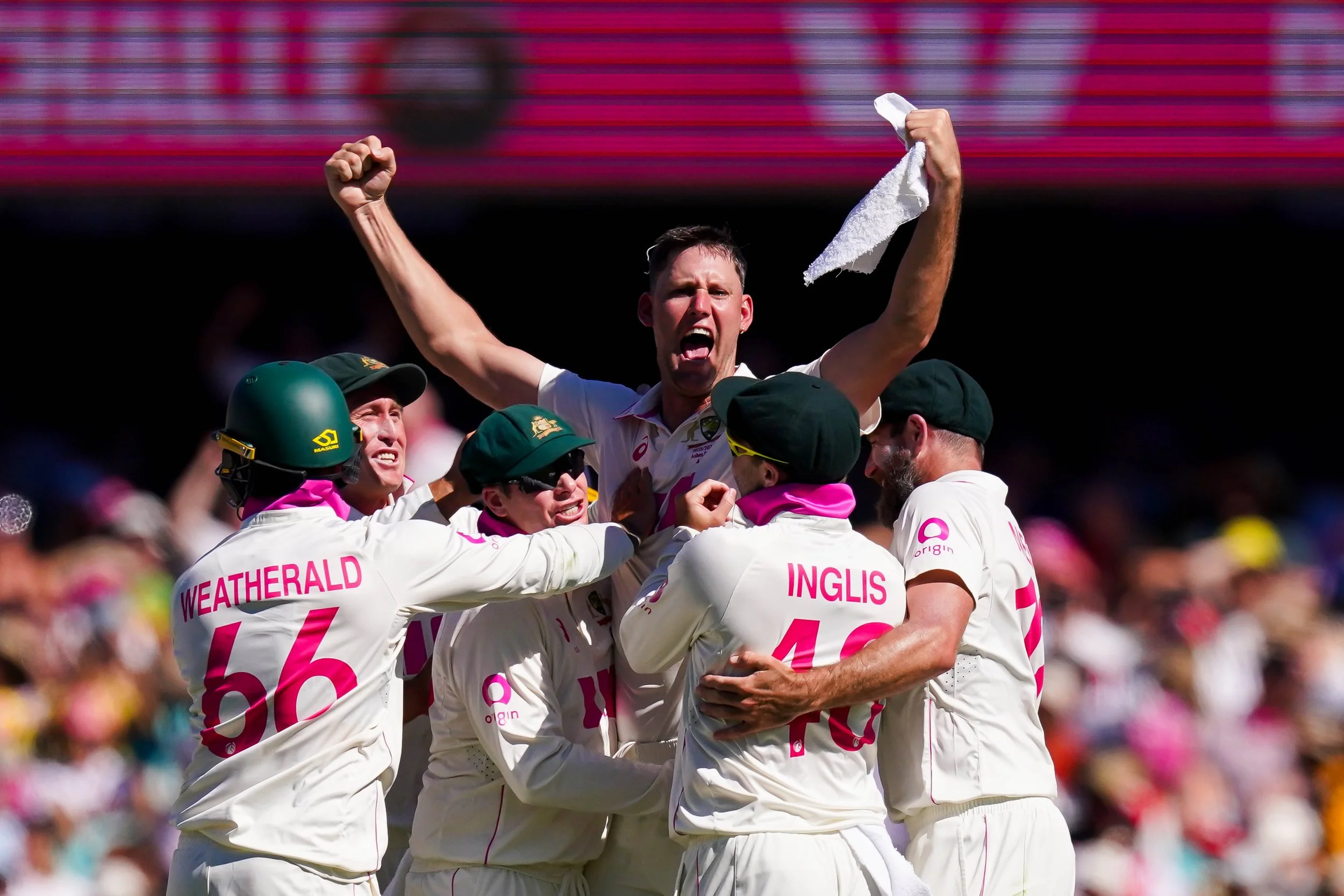 Australian cricket team celebrating victory on the field during a match, with one player raising his fist in triumph.