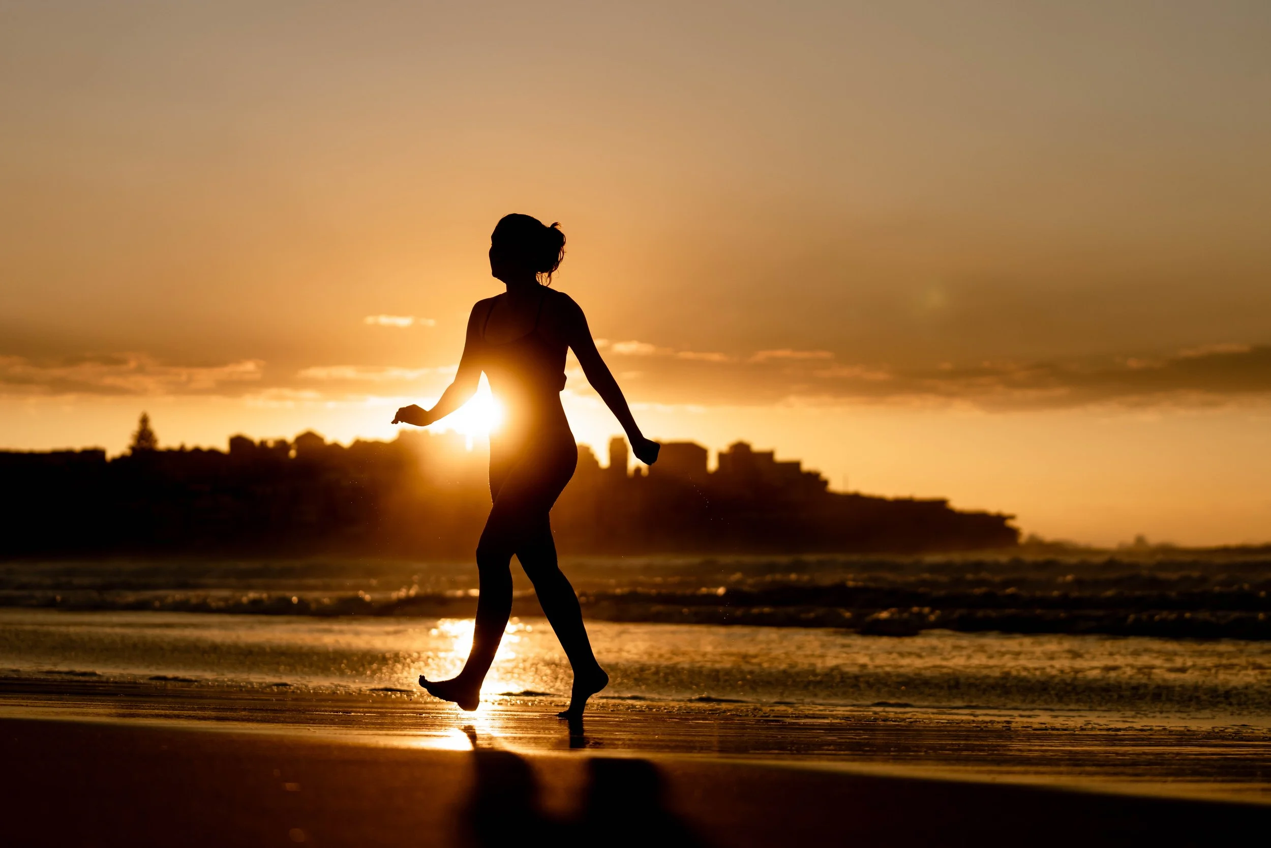 A silhouetted women leaves the sea at sunrise at Bondi Beach, Sydney, Australia